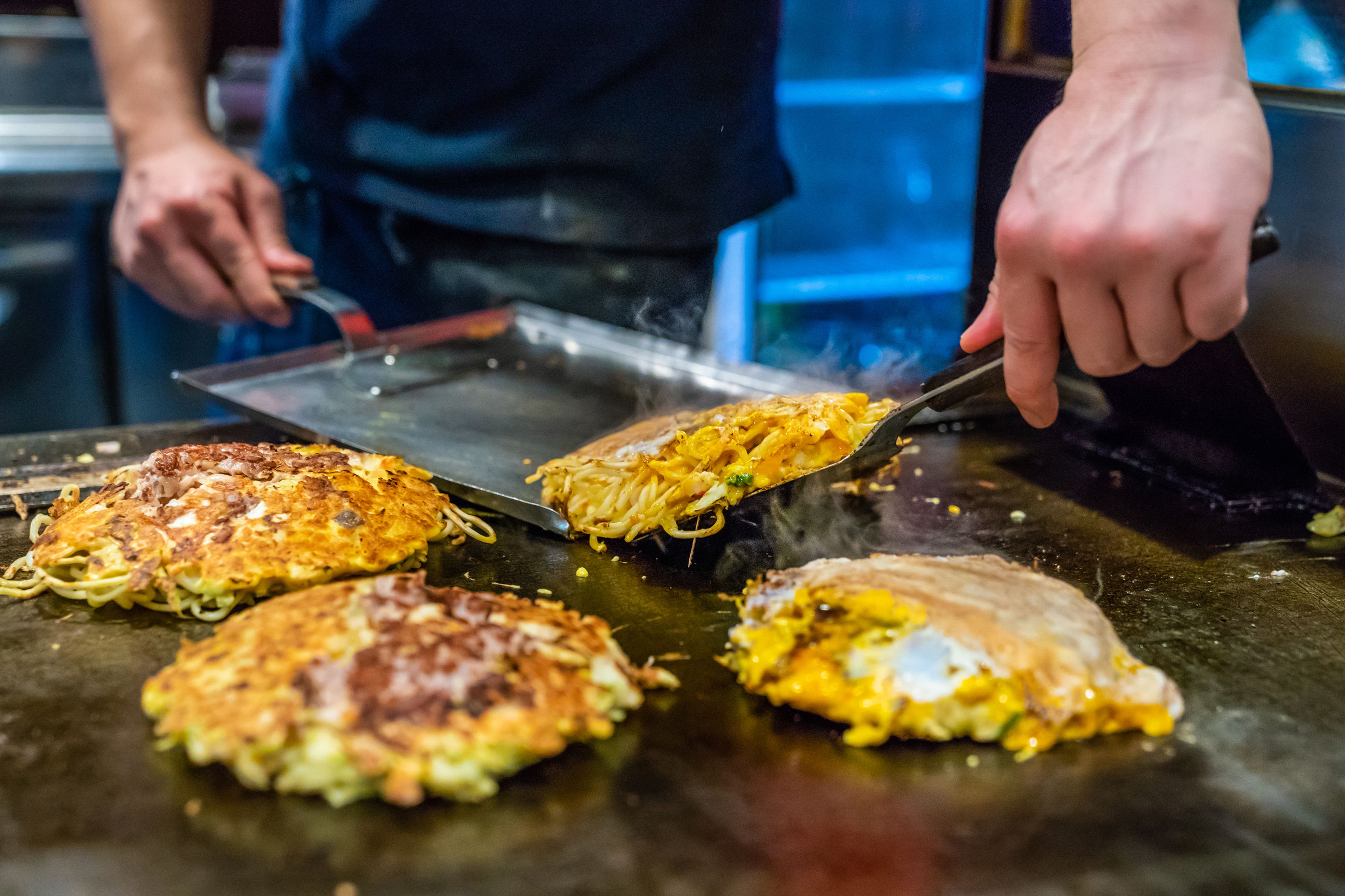 Chef preparando okonomiyaki a la plancha.