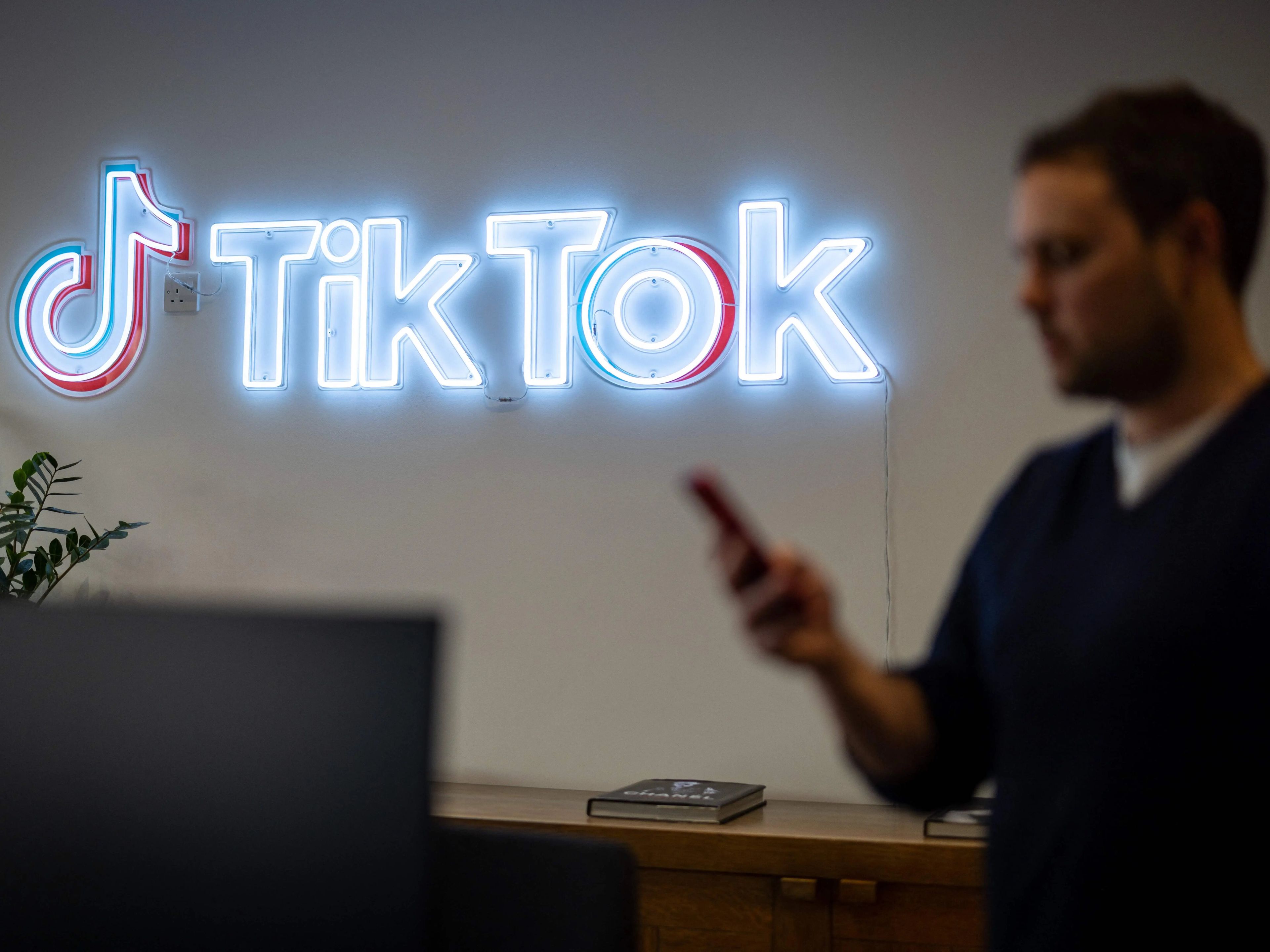 Un empleado de TikTok mira su teléfono móvil mientras pasa por delante del logotipo de TikTok en una oficina de Londres el 9 de febrero de 2022.