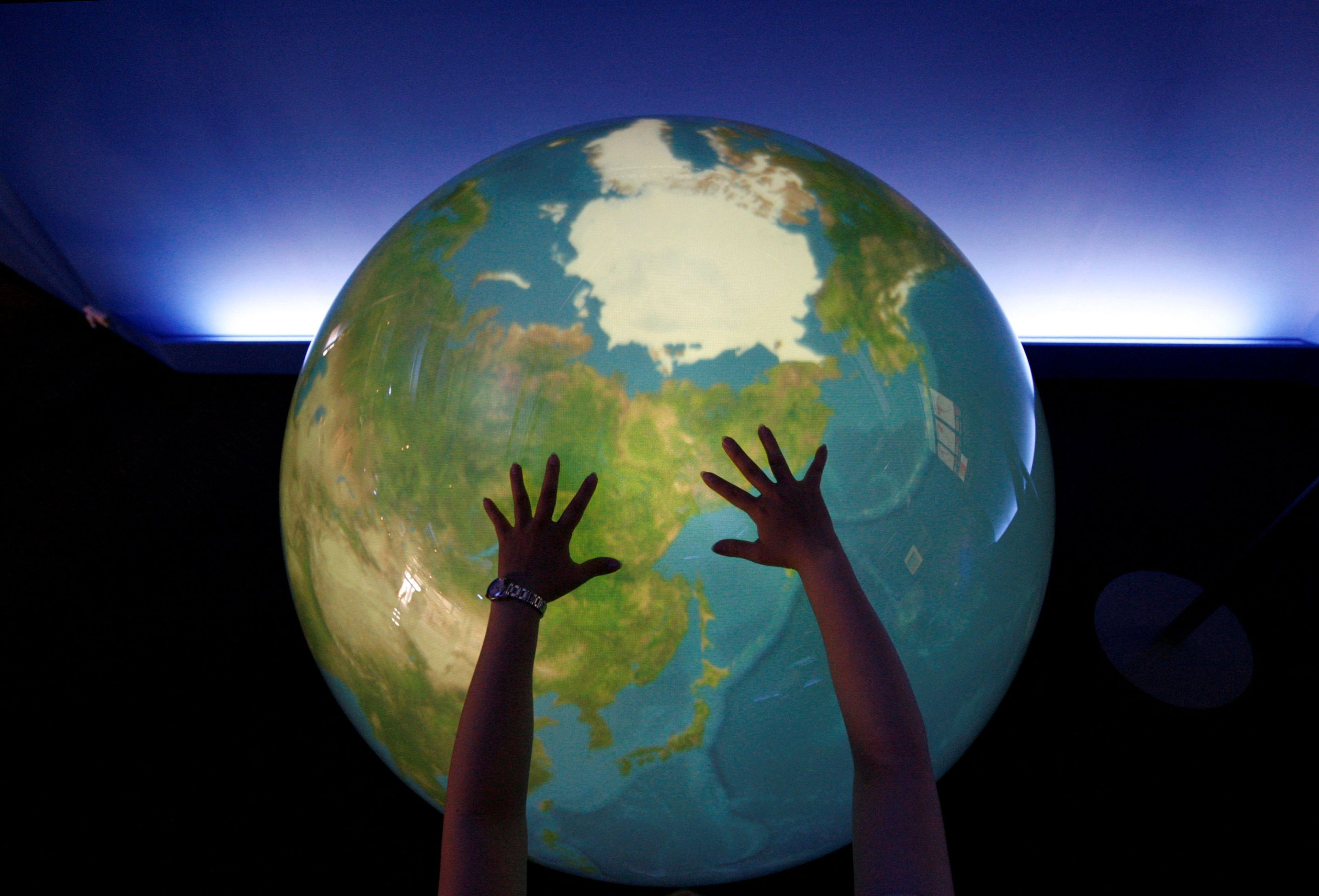 Una visitante coloca sus manos sobre un globo digital de la Tierra en una exhibición en Rusutsu (Japón).
