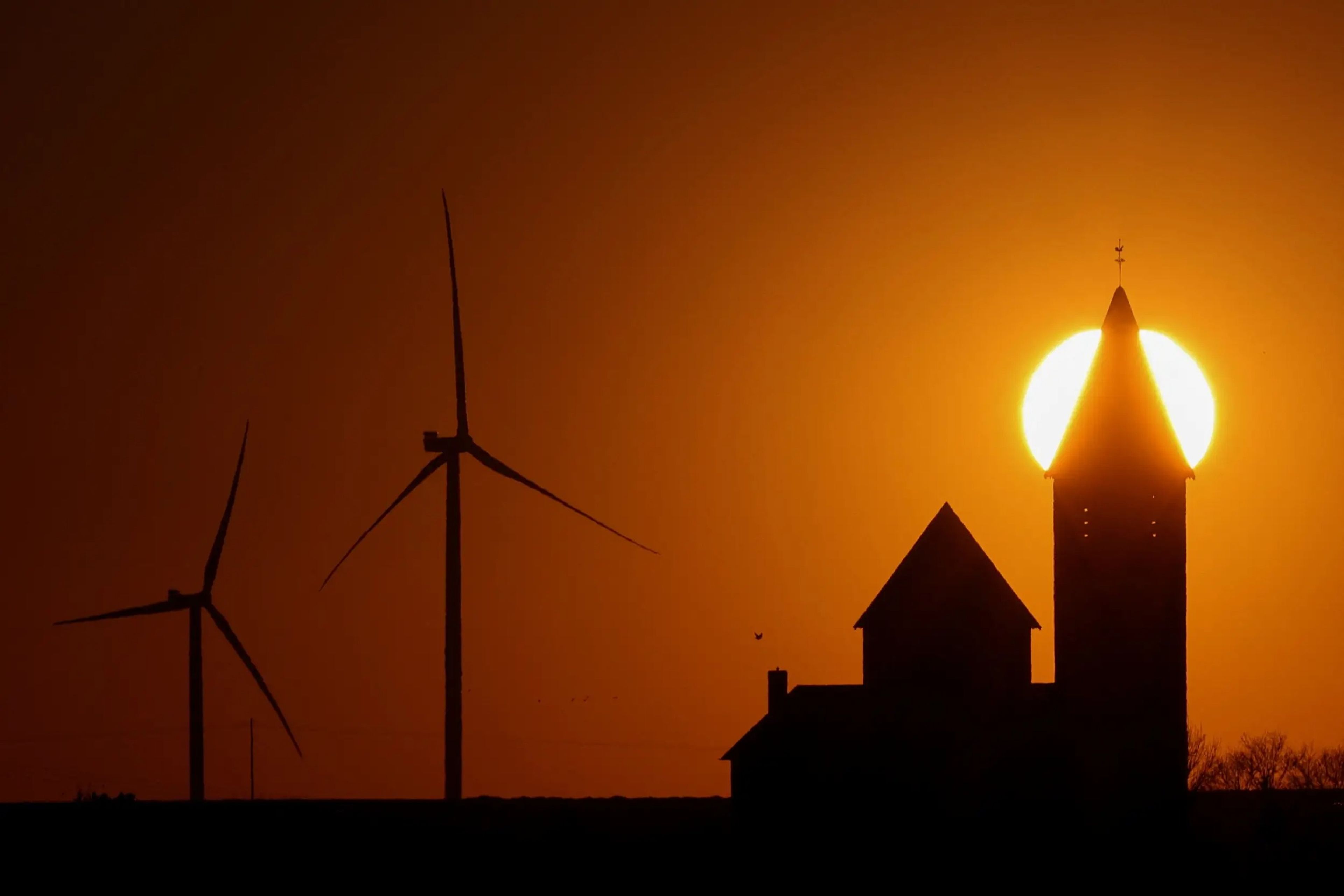 Turbinas de molinos de viento que generan energía junto a una iglesia en el pueblo de Noreuil durante la puesta de sol en un parque eólico cerca de Cambrai (Francia), el 18 de marzo de 2022.