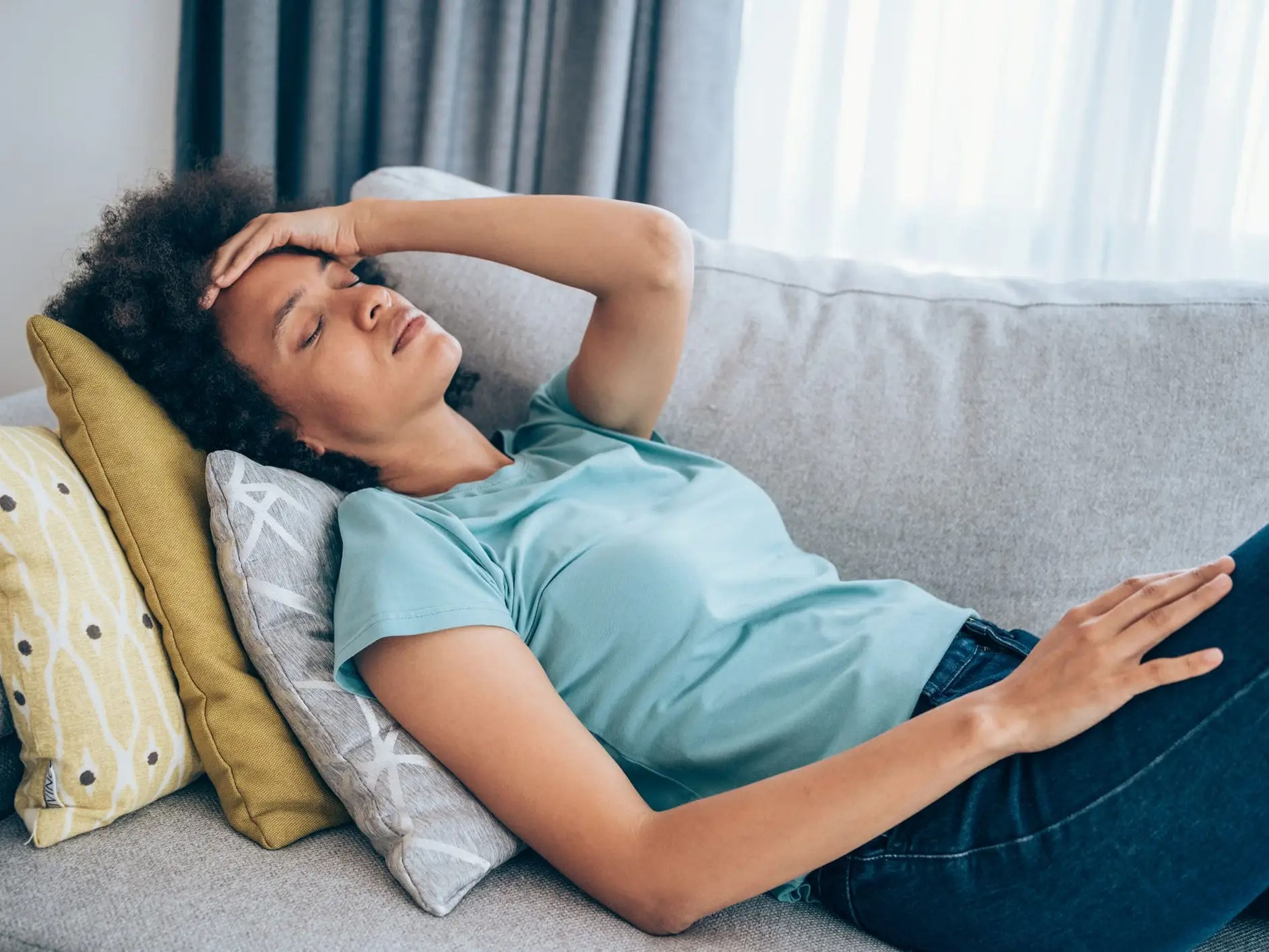 a woman laying on a couch looking ill and putting her hand to her forehead