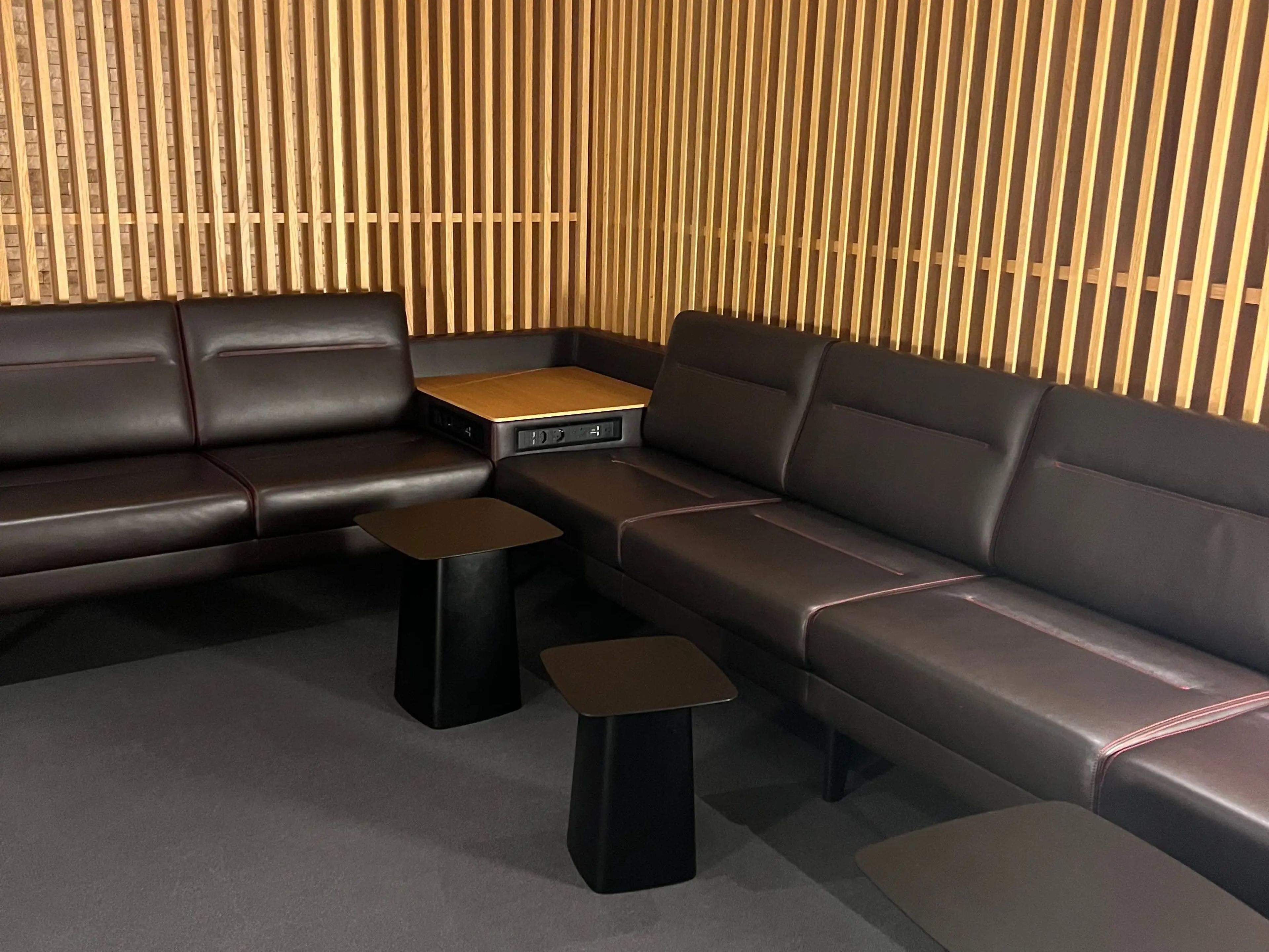 an airport lounge with sleek black couches, small tables, and a wood panel wall