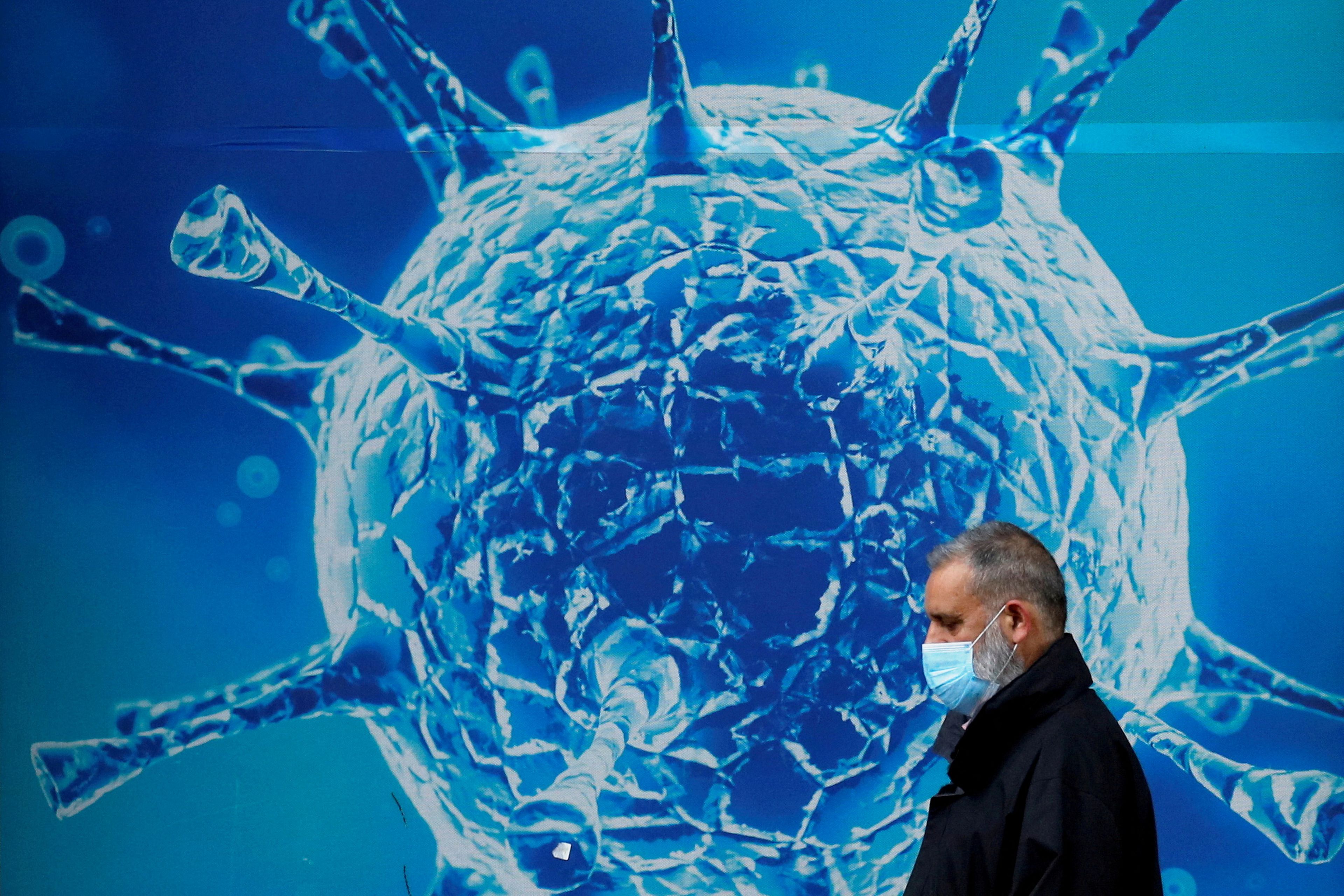 Hombre con mascarilla pasa delante de imagen de virus, en pandemia por covid-19