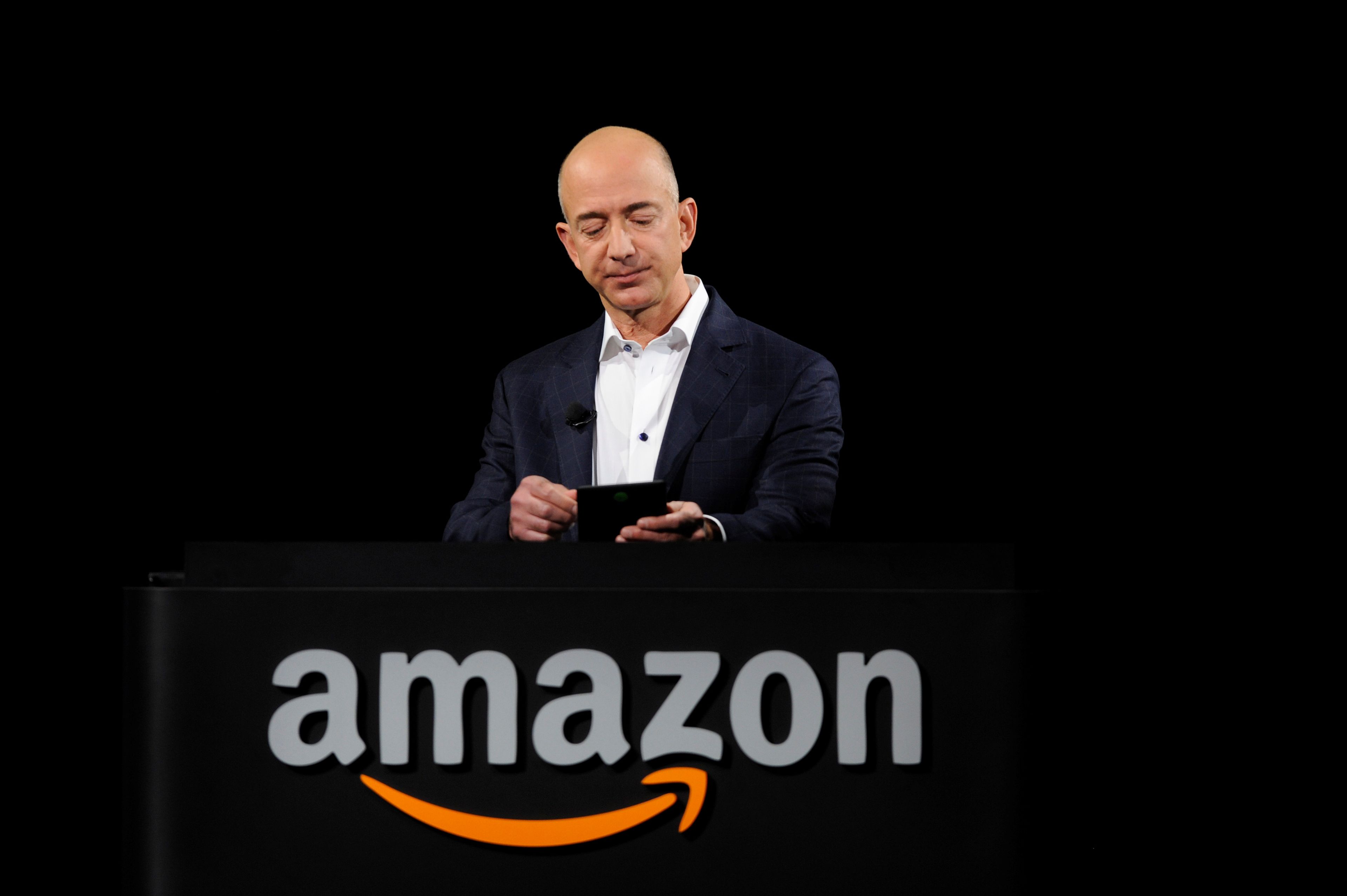 Jeff Bezos, con un Kindle, detrás de un logo de Amazon