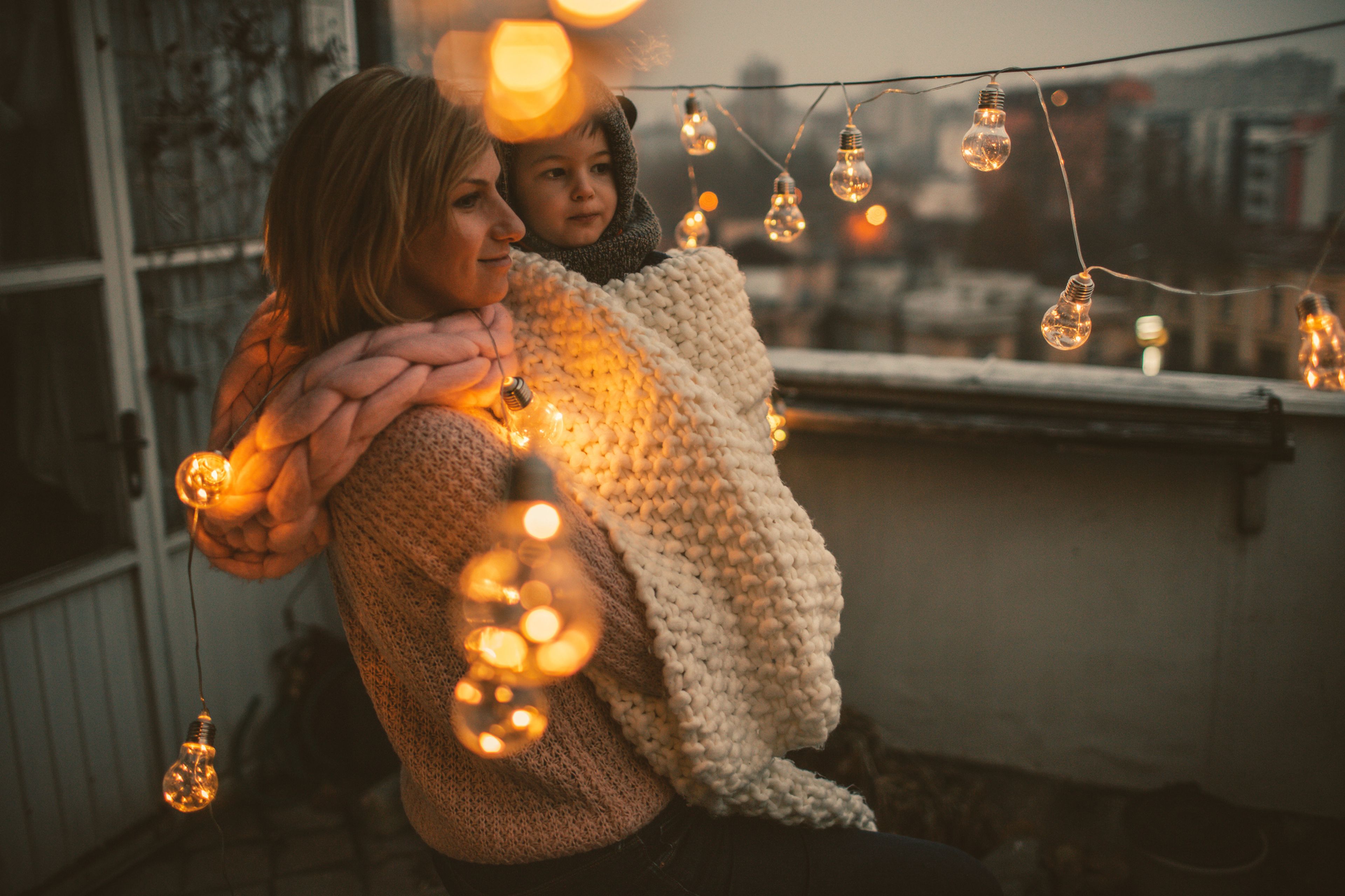 Madre e hija en una terraza con bombillas.