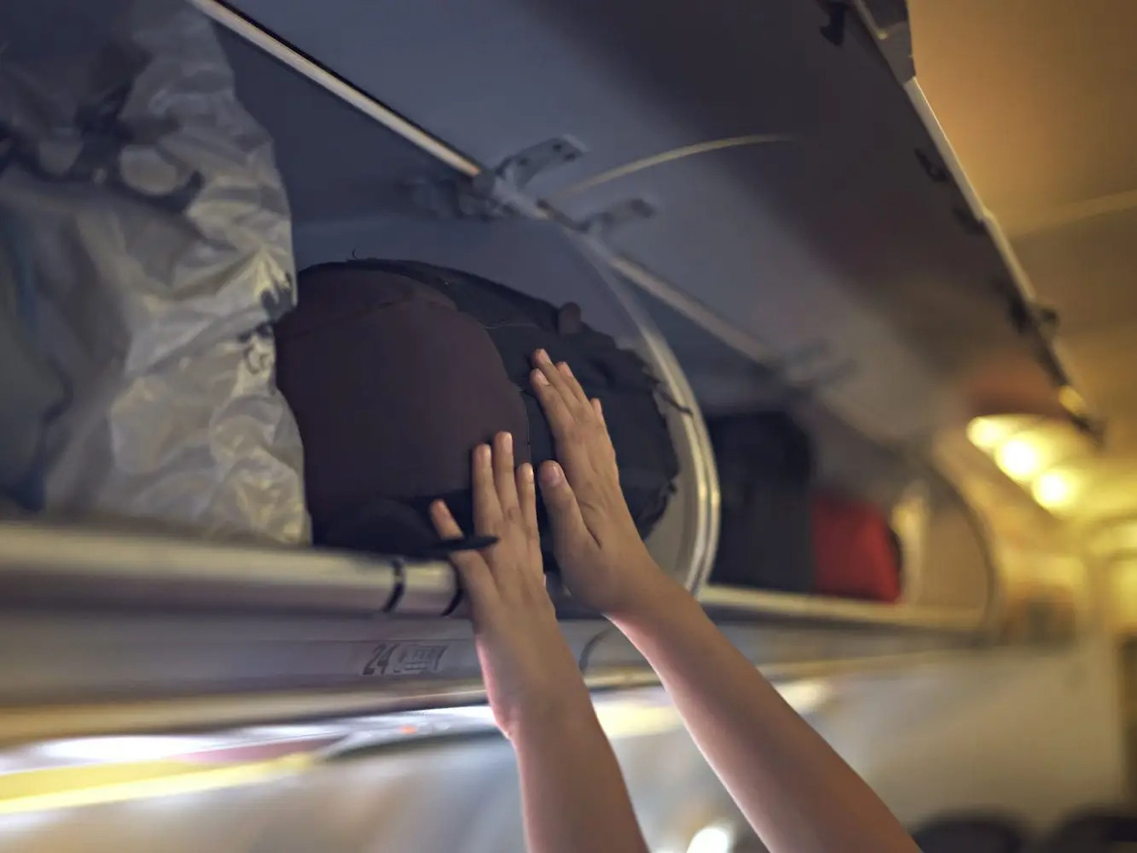 A person lifts their luggage into an overhead bin.