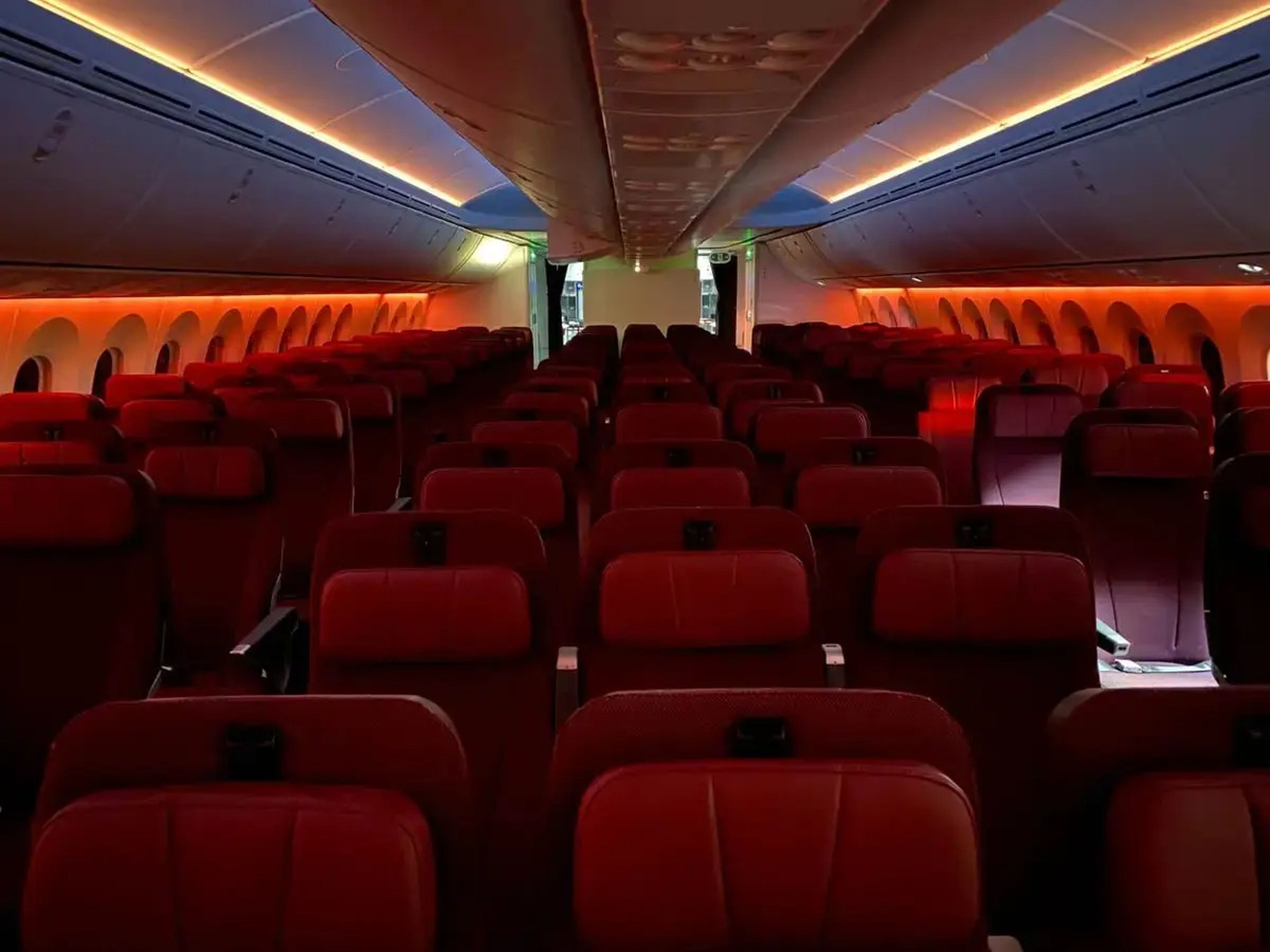 Red and orange lights dimmed above an empty row of seats on a plane.