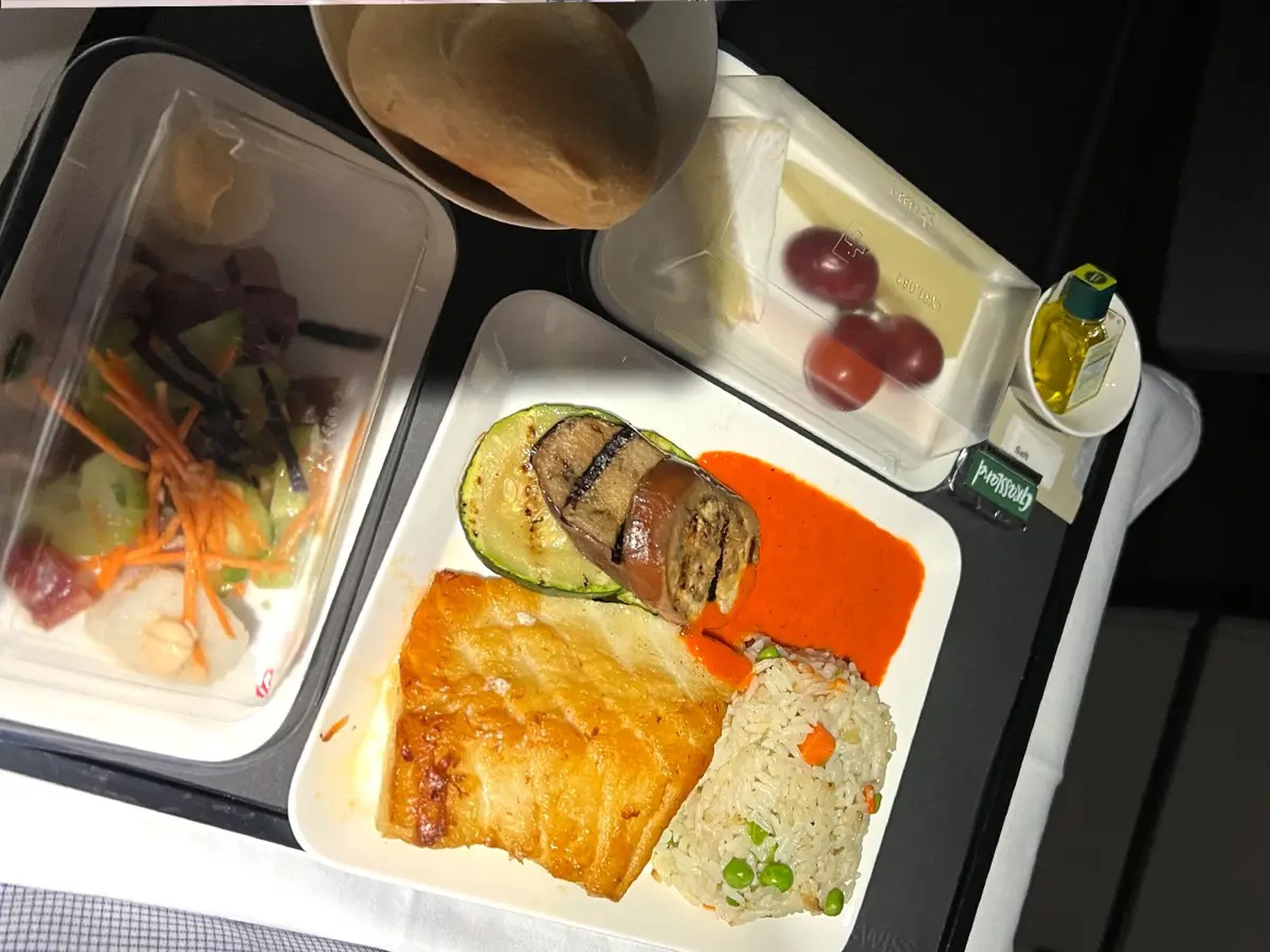 A tray of food on a plane with fish, rice, and grapes