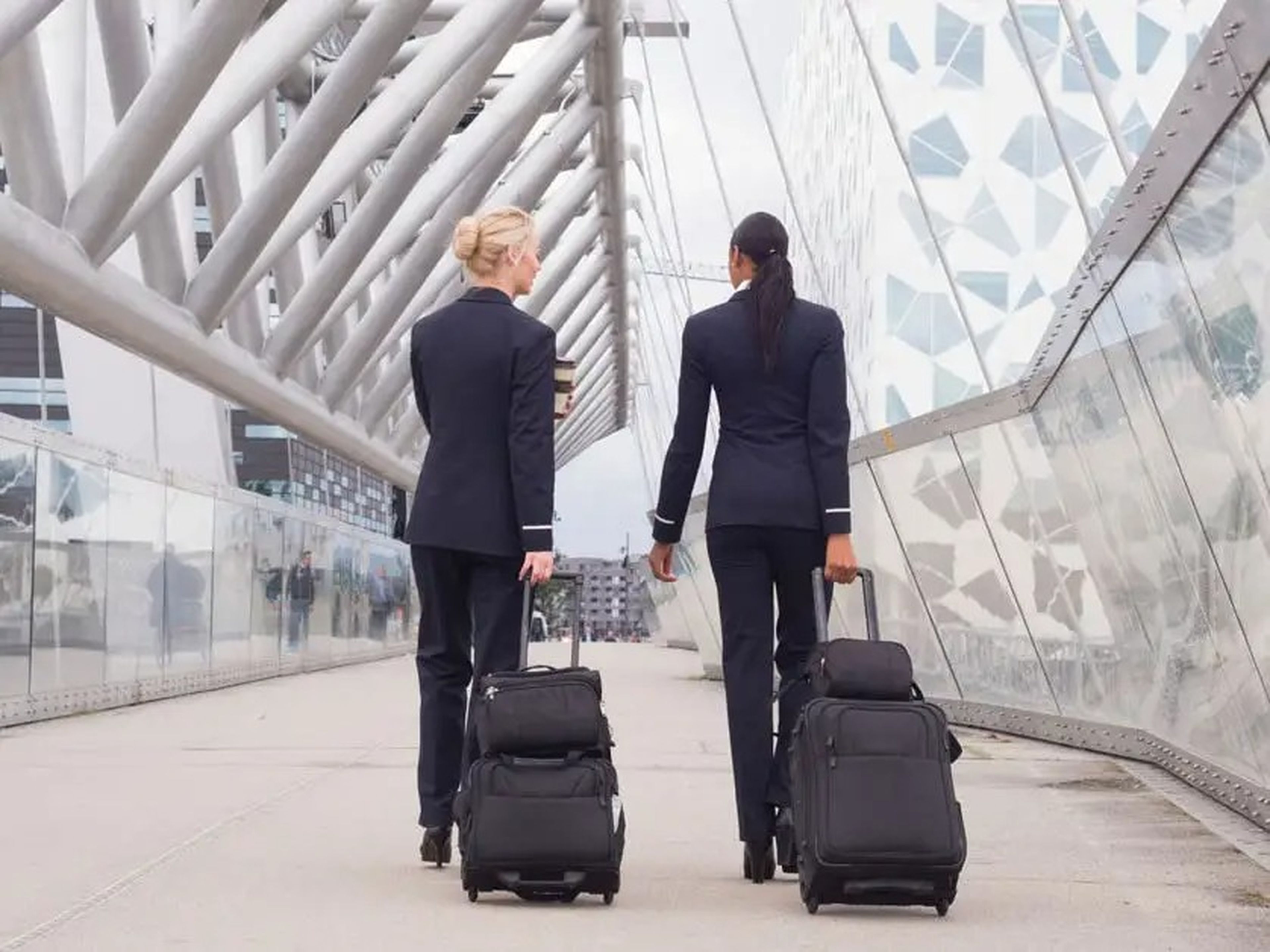 Two feminine flight attendants walking in the airport with suitcases