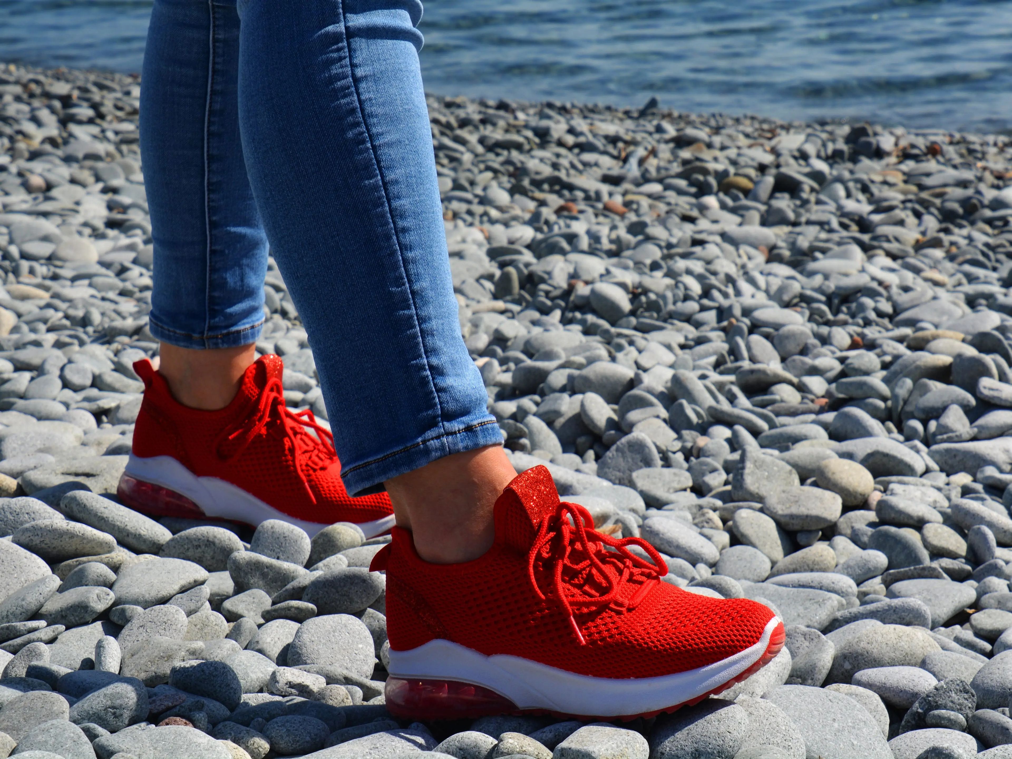 Woman wearing jeans and red sneakers on rocky beach