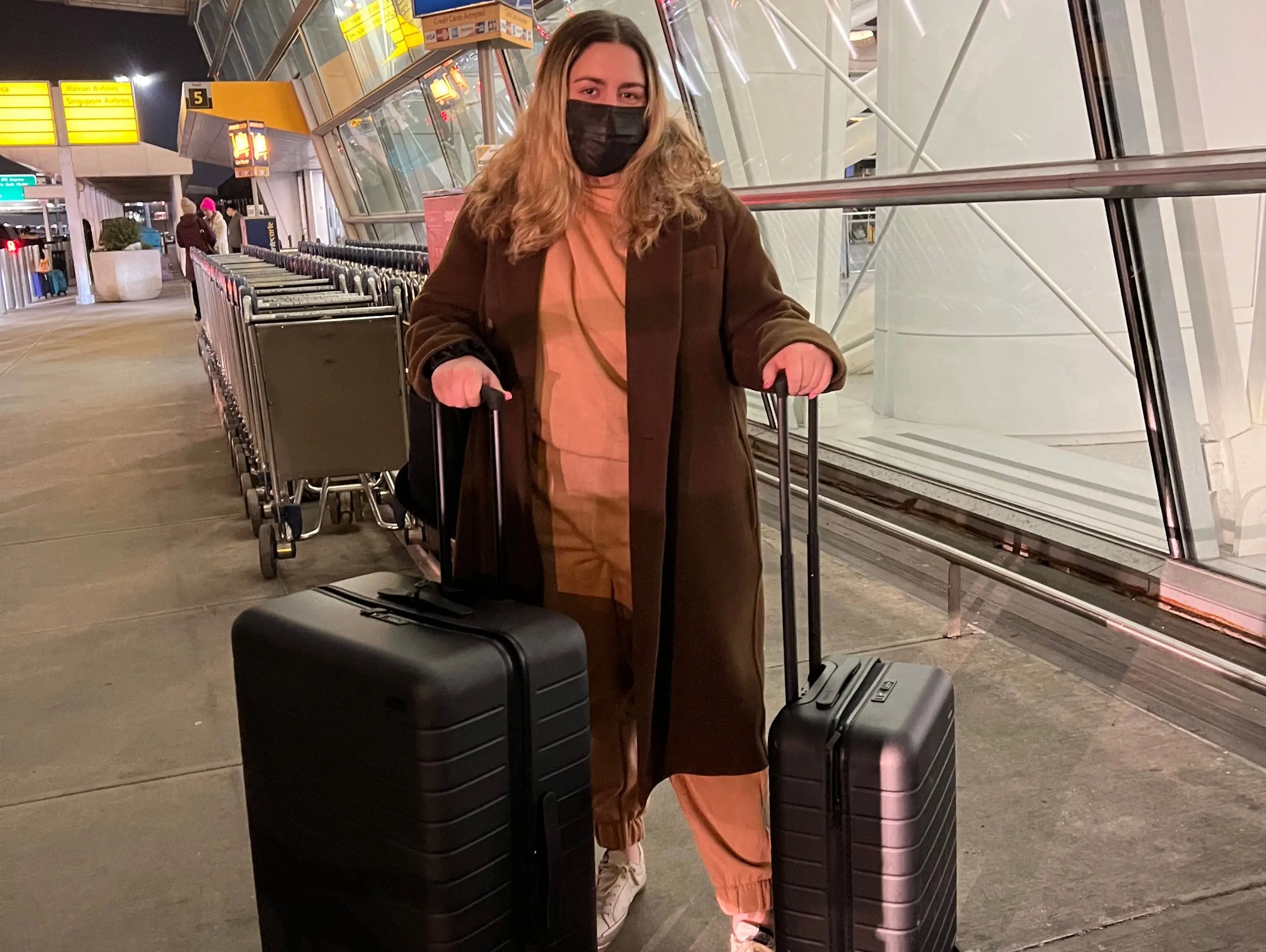 The writer with two suitcases and a mask on, leaving for her trip at the airport.