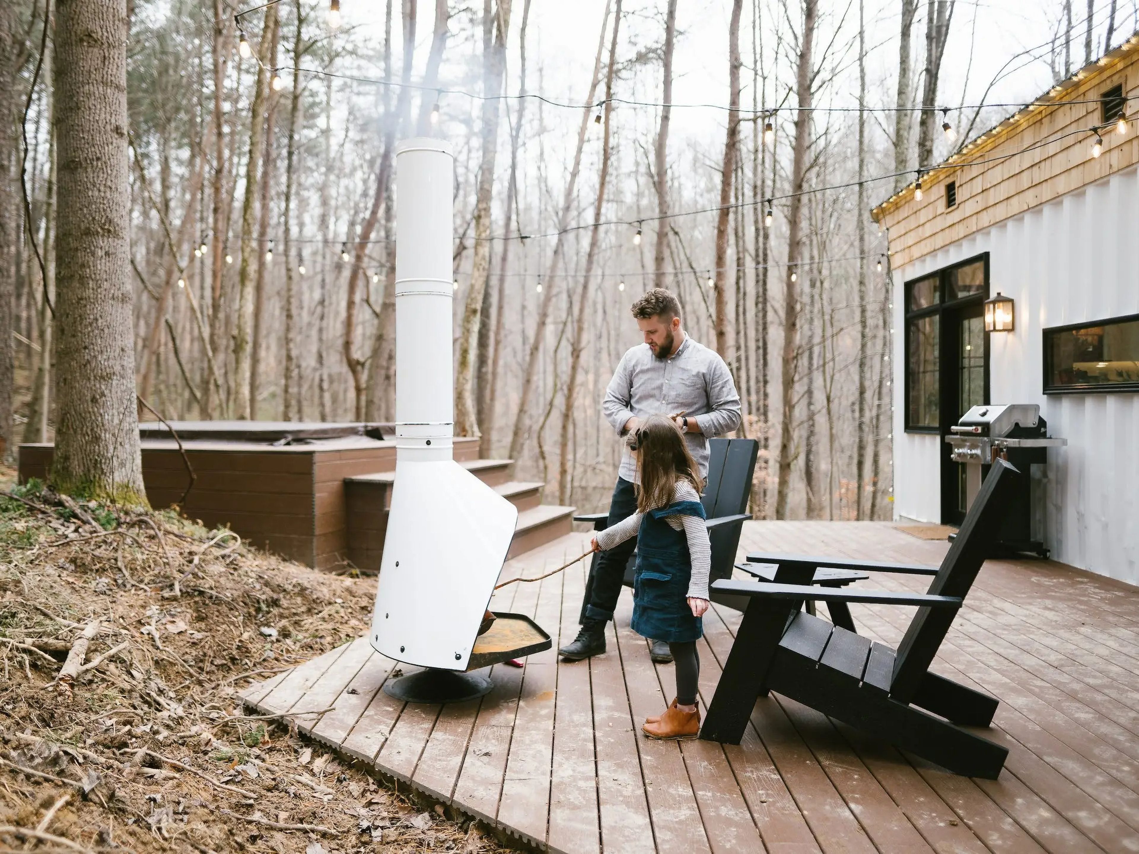 An adult and child near an outdoor fire pit next to a shipping container home.