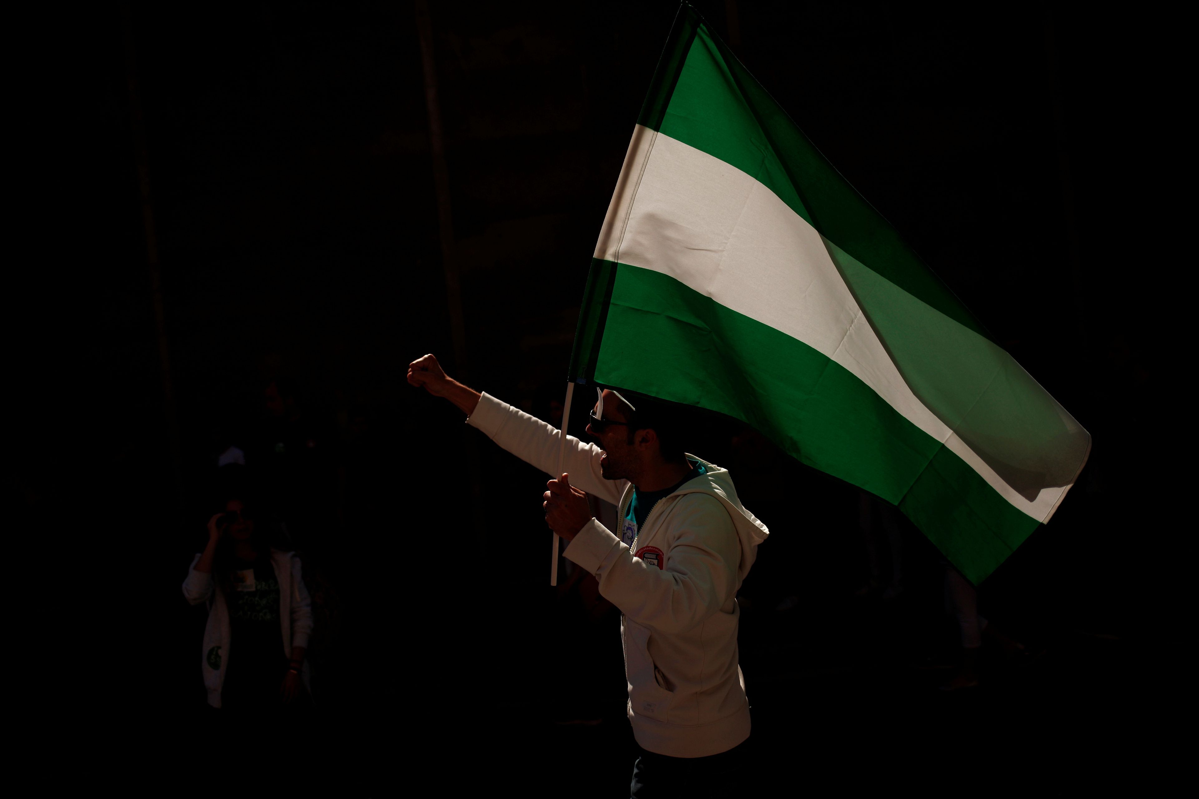 Un hombre en una manifestación con una bandera de Andalucía.