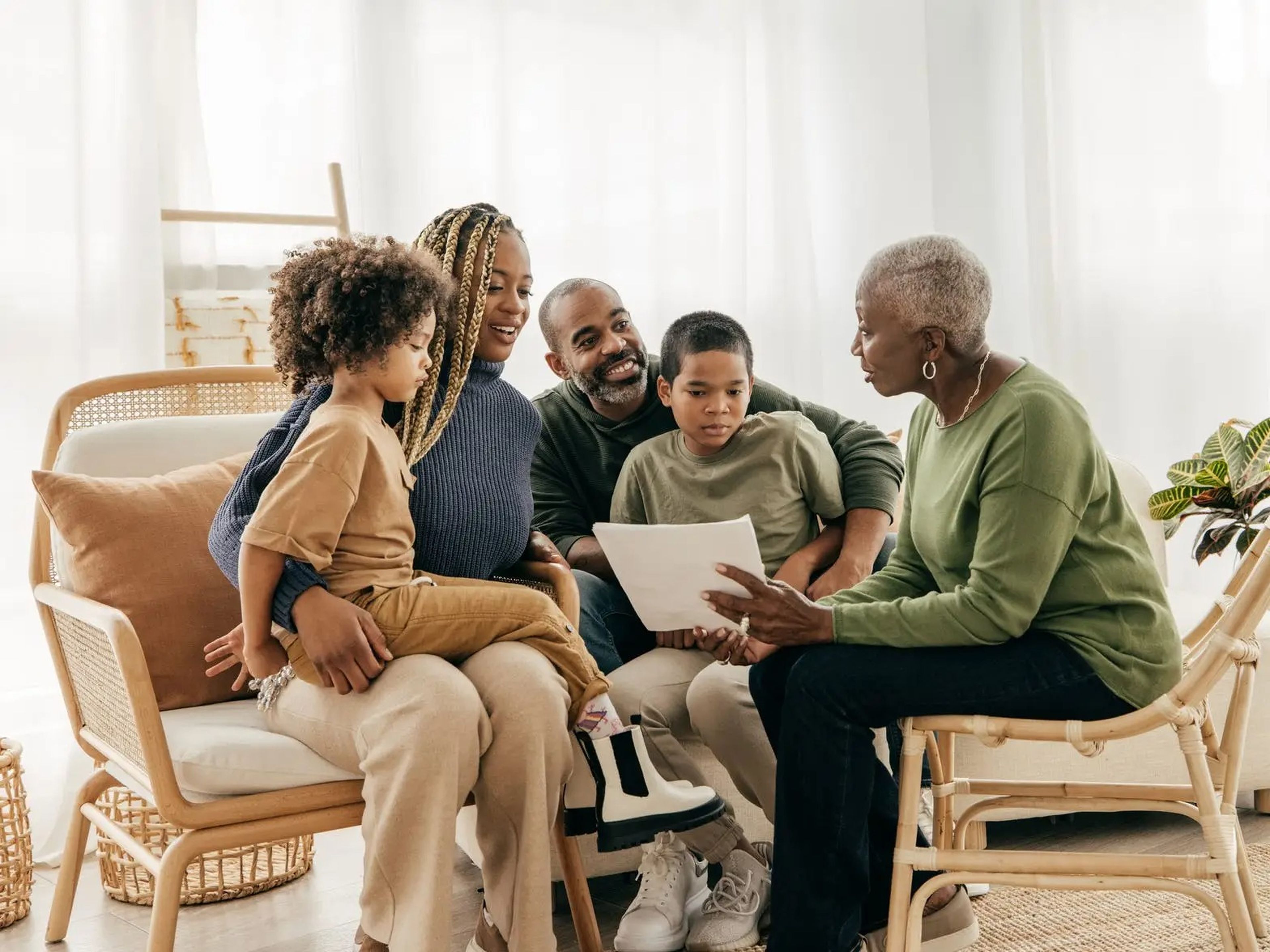an intergenerational Black family seated together in a well-lit living room looking at a piece of paper