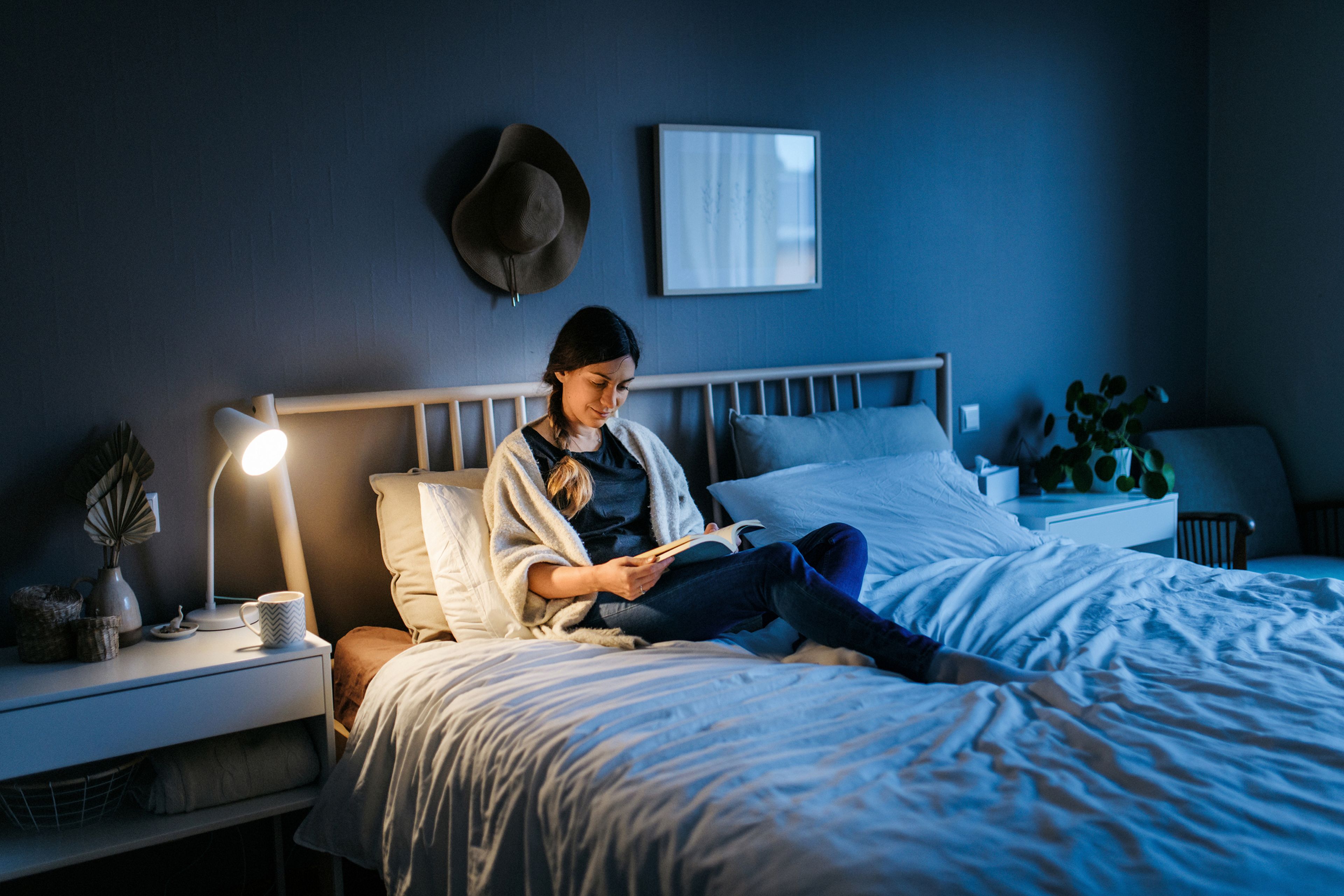 Una mujer leyendo un libro en la cama con la lámpara encendida