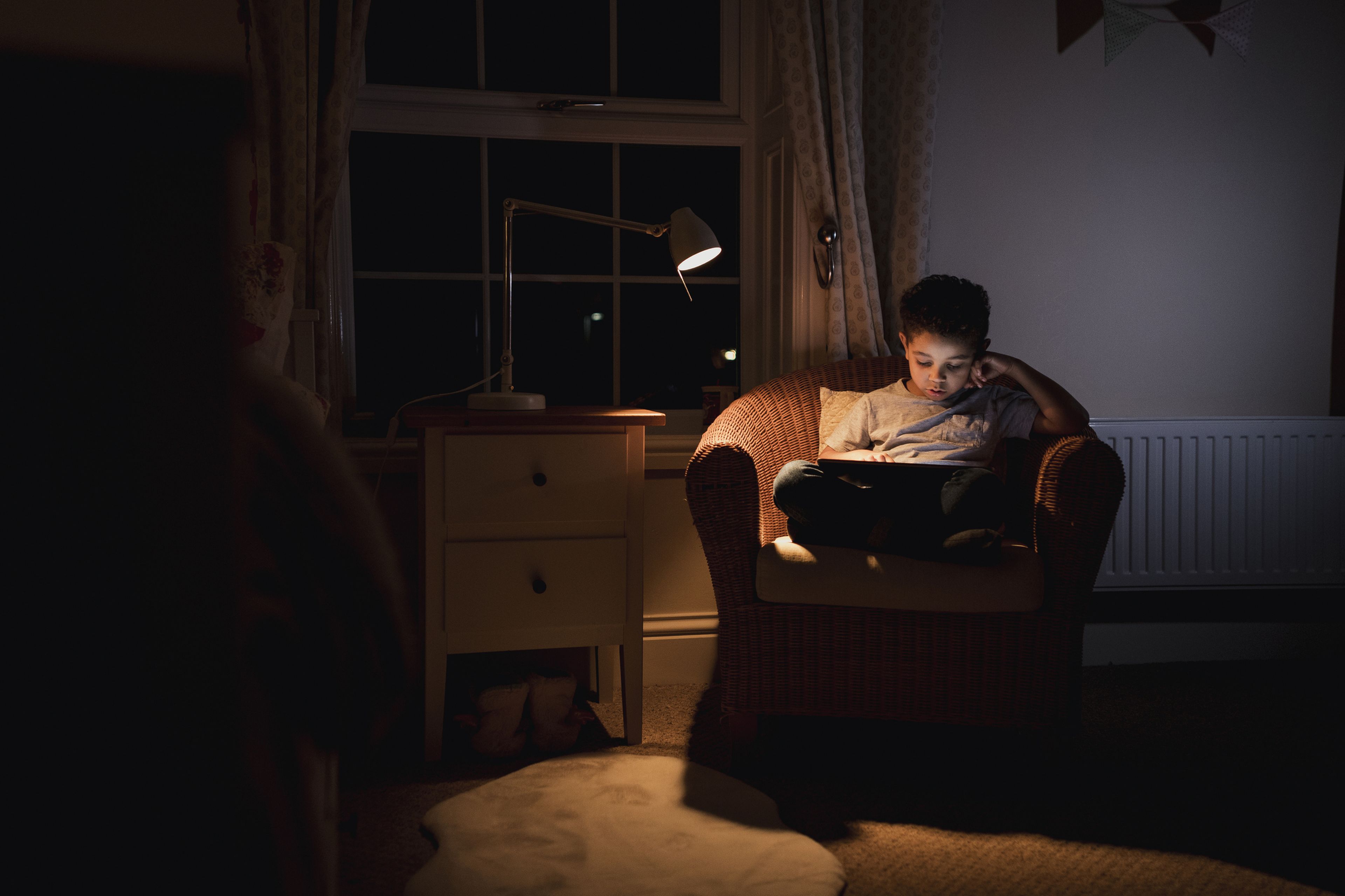 Un niño mira una tablet bajo la luz de una lámpara.