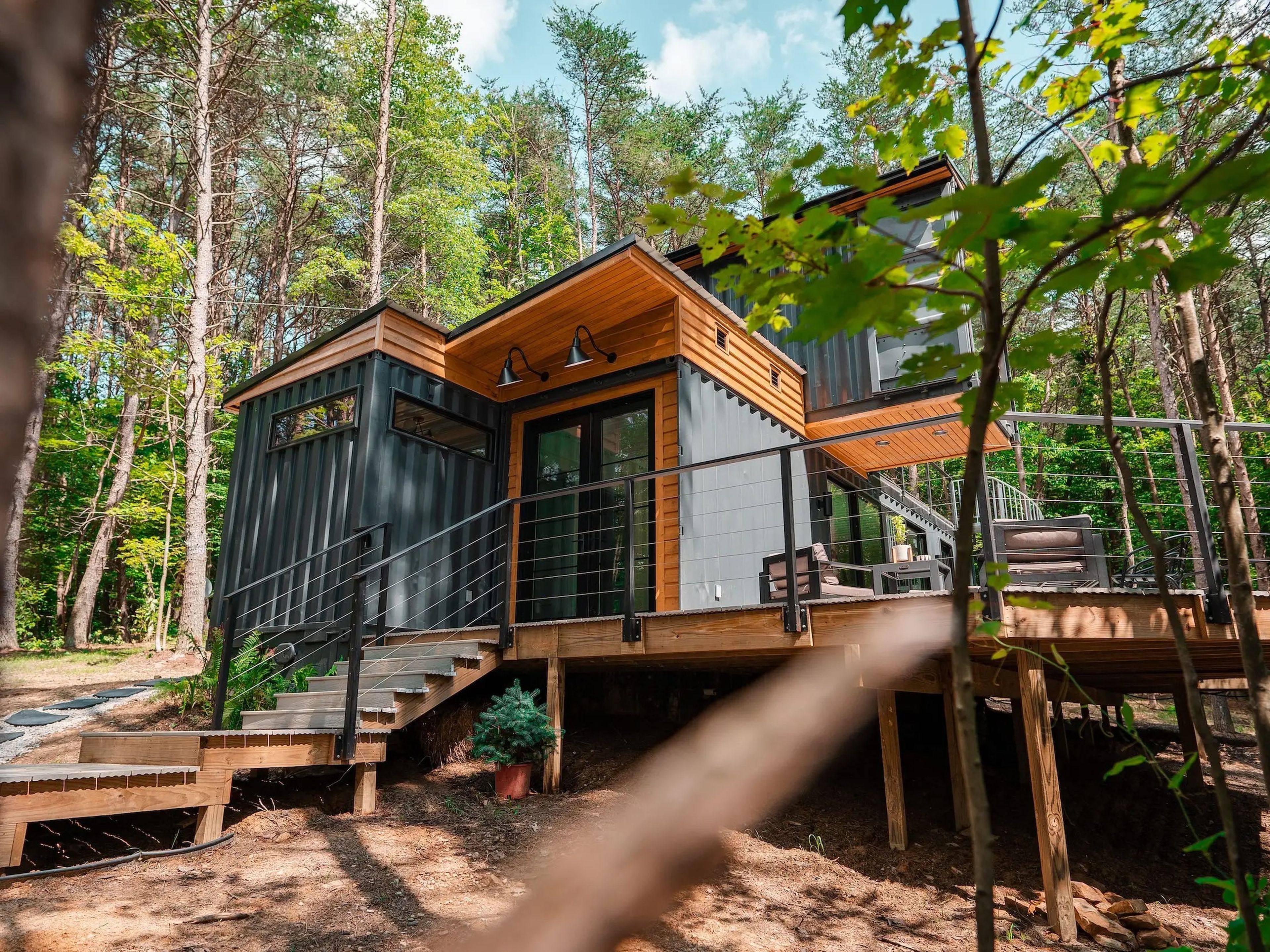 The OG Box, a shipping container home, surrounded by trees on a bright day.