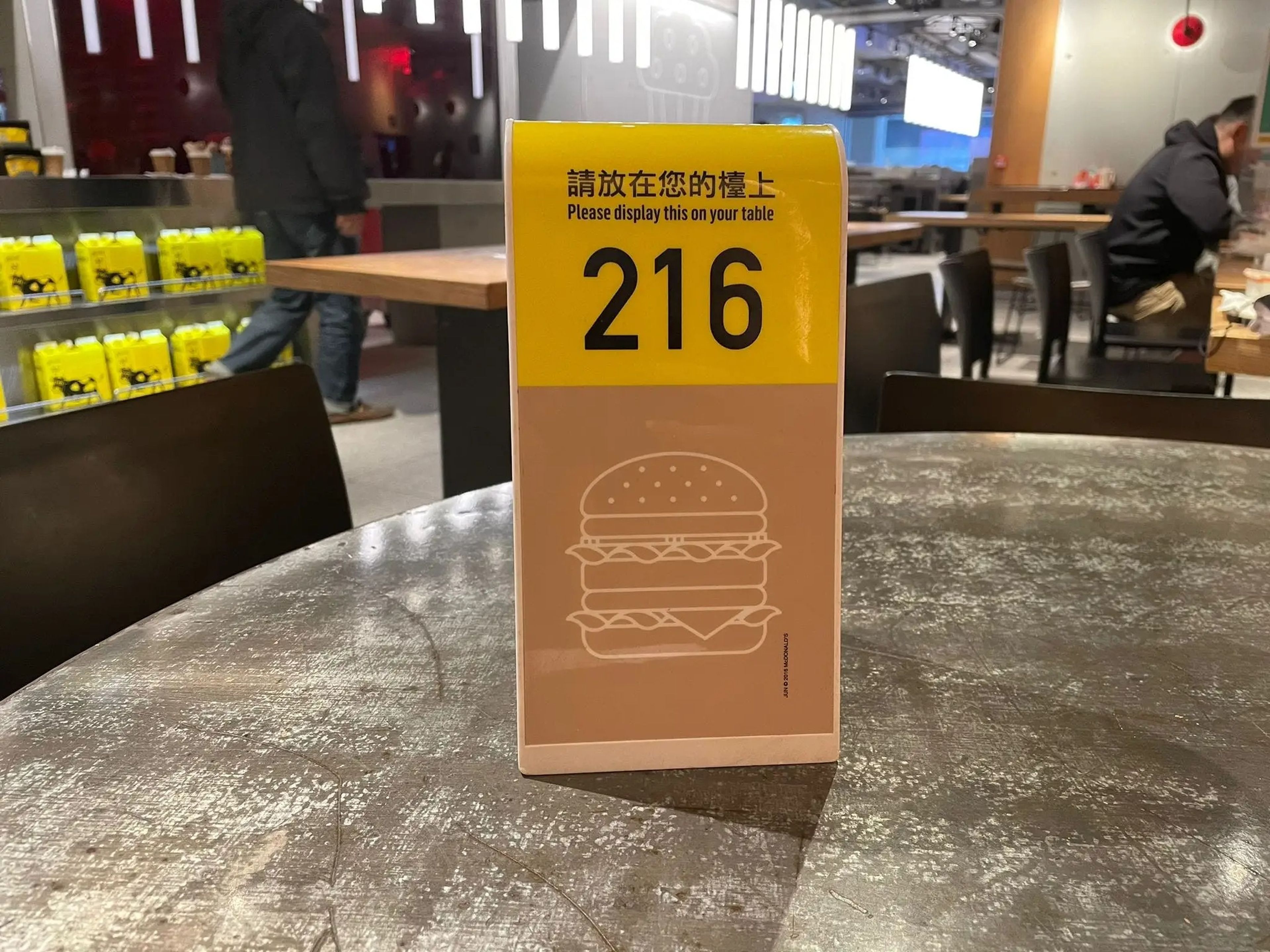 A plastic marker on a table with a brown illustration with a burger on it and the number "216" printed on it