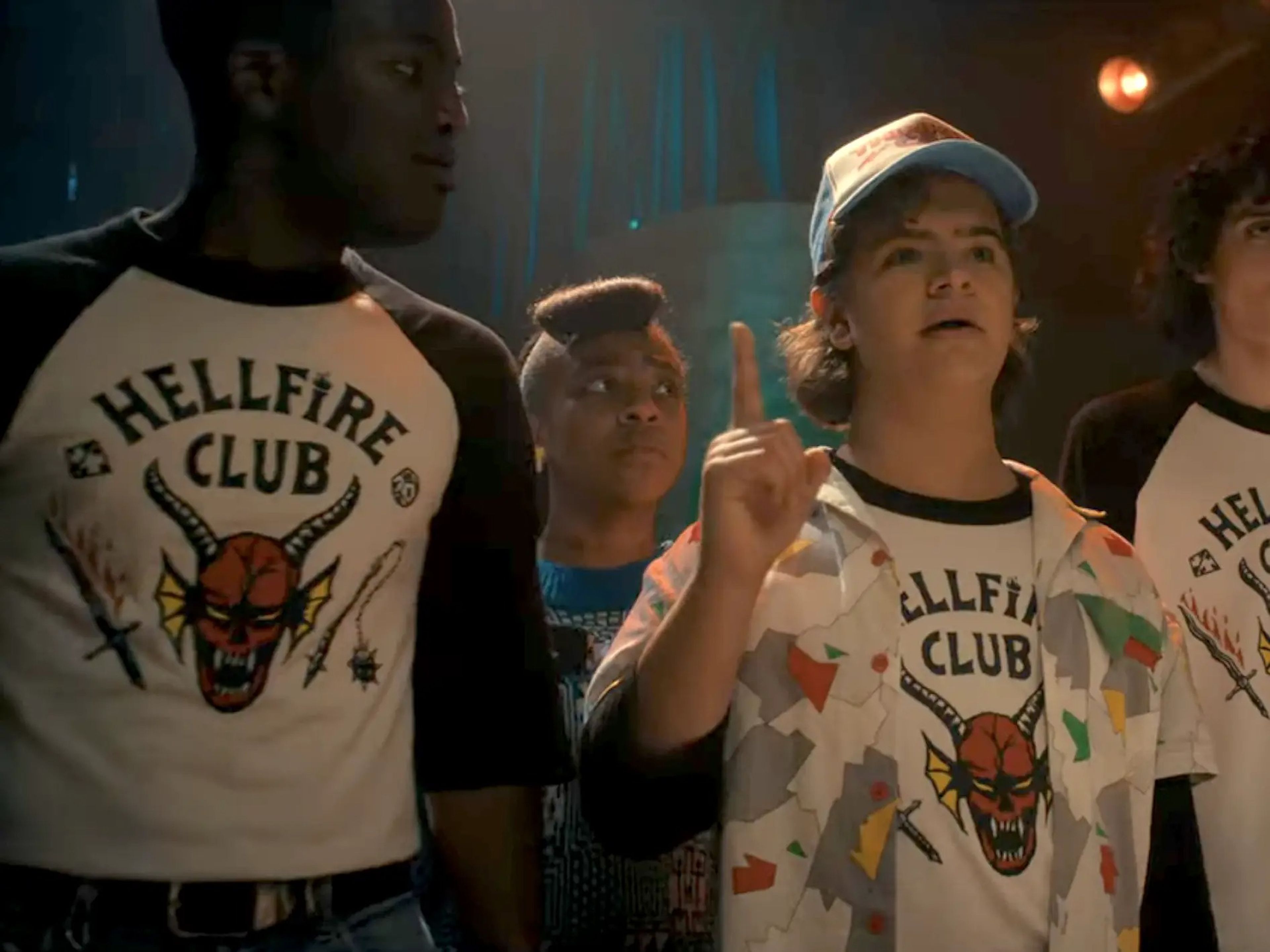 A scene from Netflix's sci-fi series "Stranger Things," showing four teenagers wearing matching shirts that say "Hellfire Club."