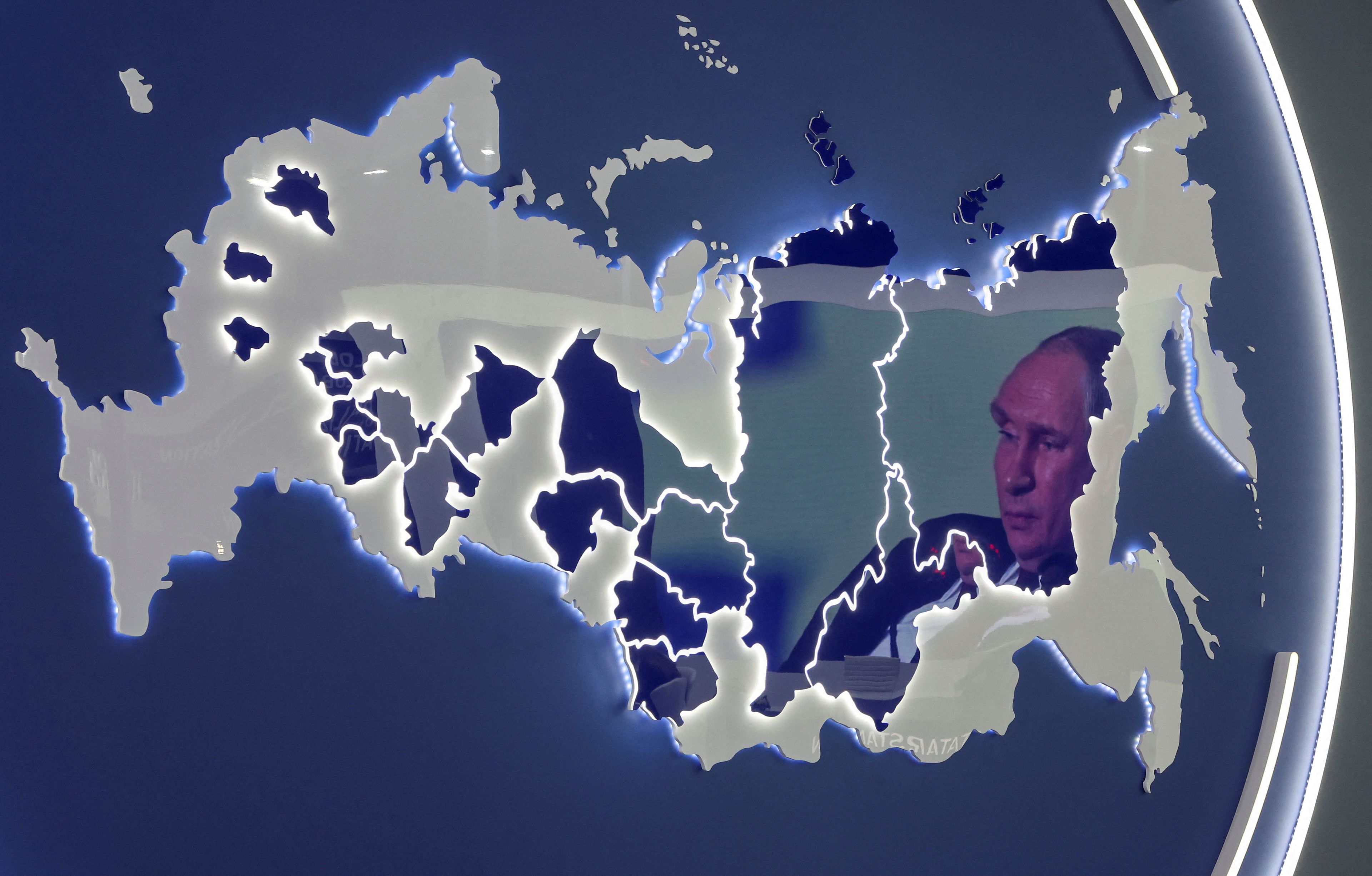 Una pantalla donde aparece el presidente ruso Vladímir Putin se refleja en un stand que muestra el mapa de Rusia.