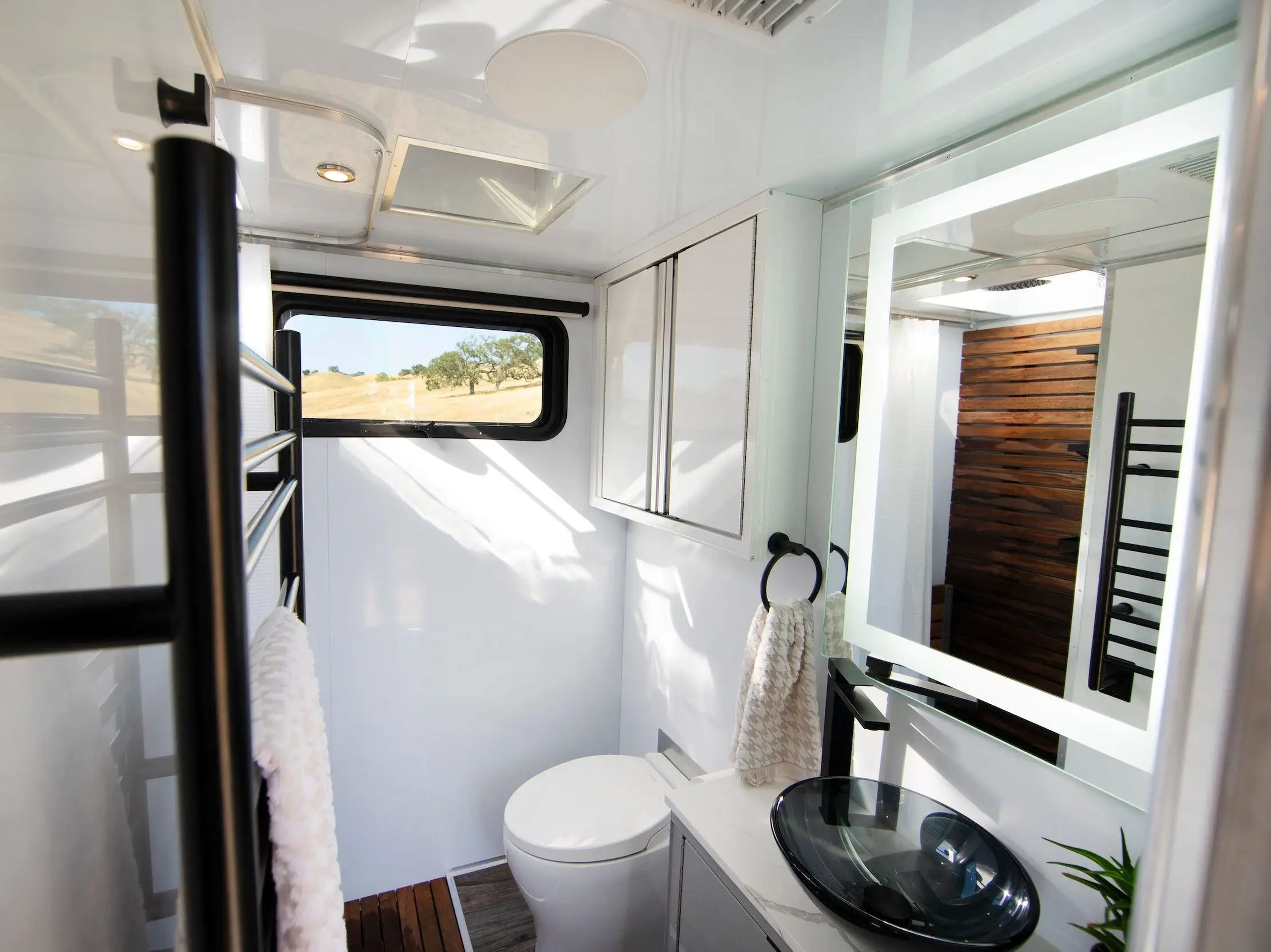 A bathroom with a window, towerl rack, mirror, sink, toilet.