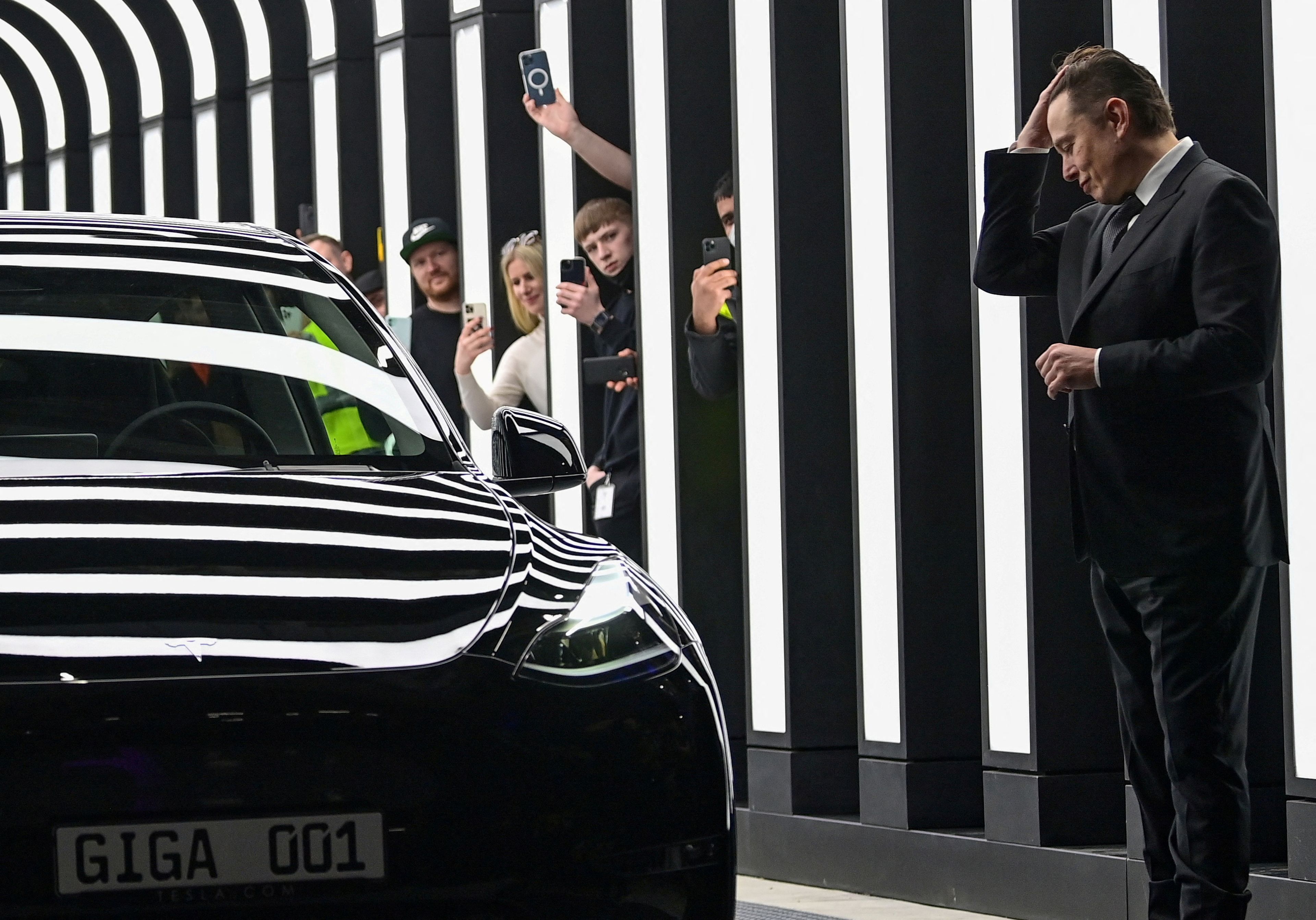 Elon Musk llevándose las manos a la cabeza frente a un Tesla.