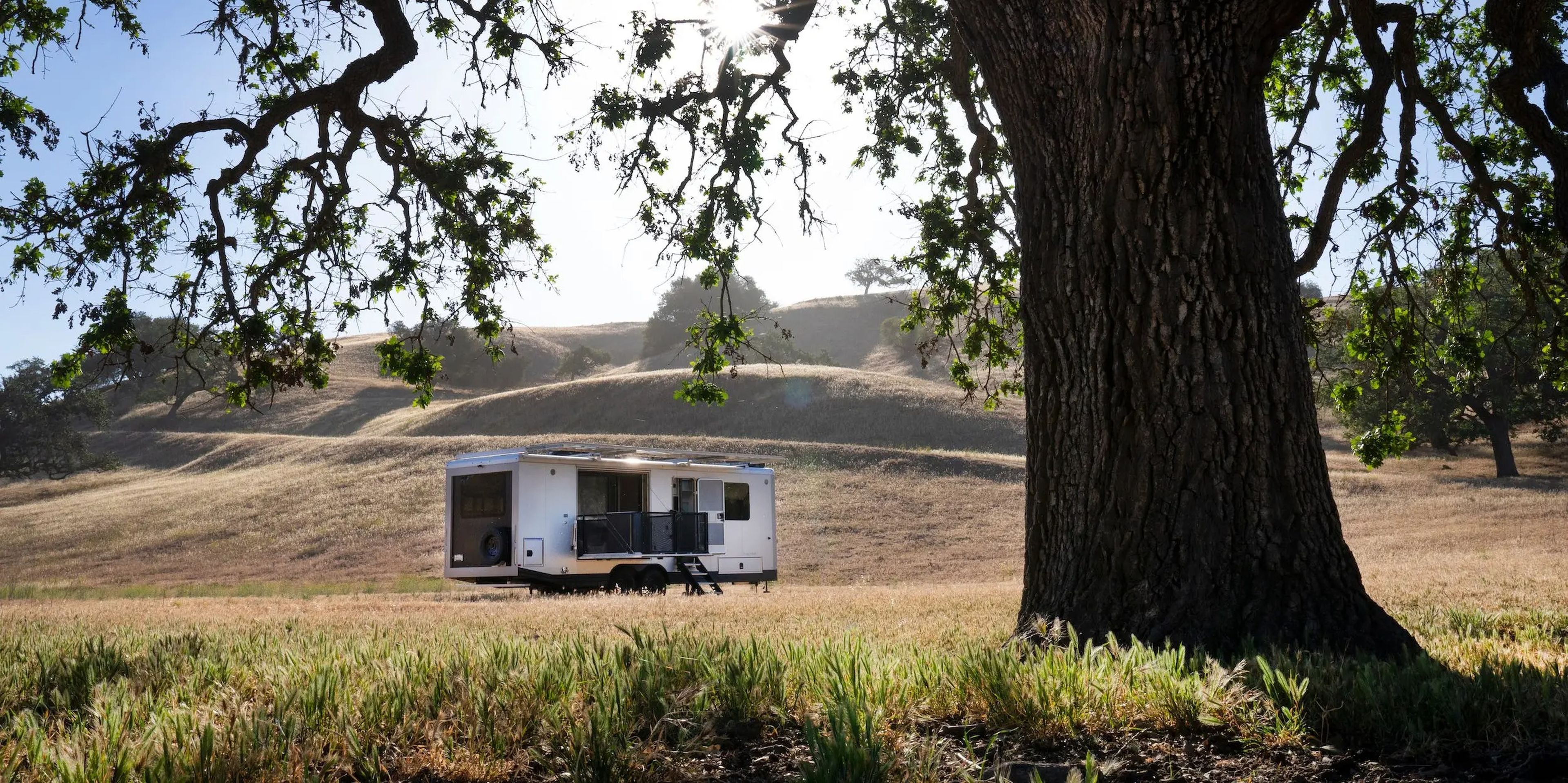 The exterior of the travel trailer as it sits on a brown field near a tree.