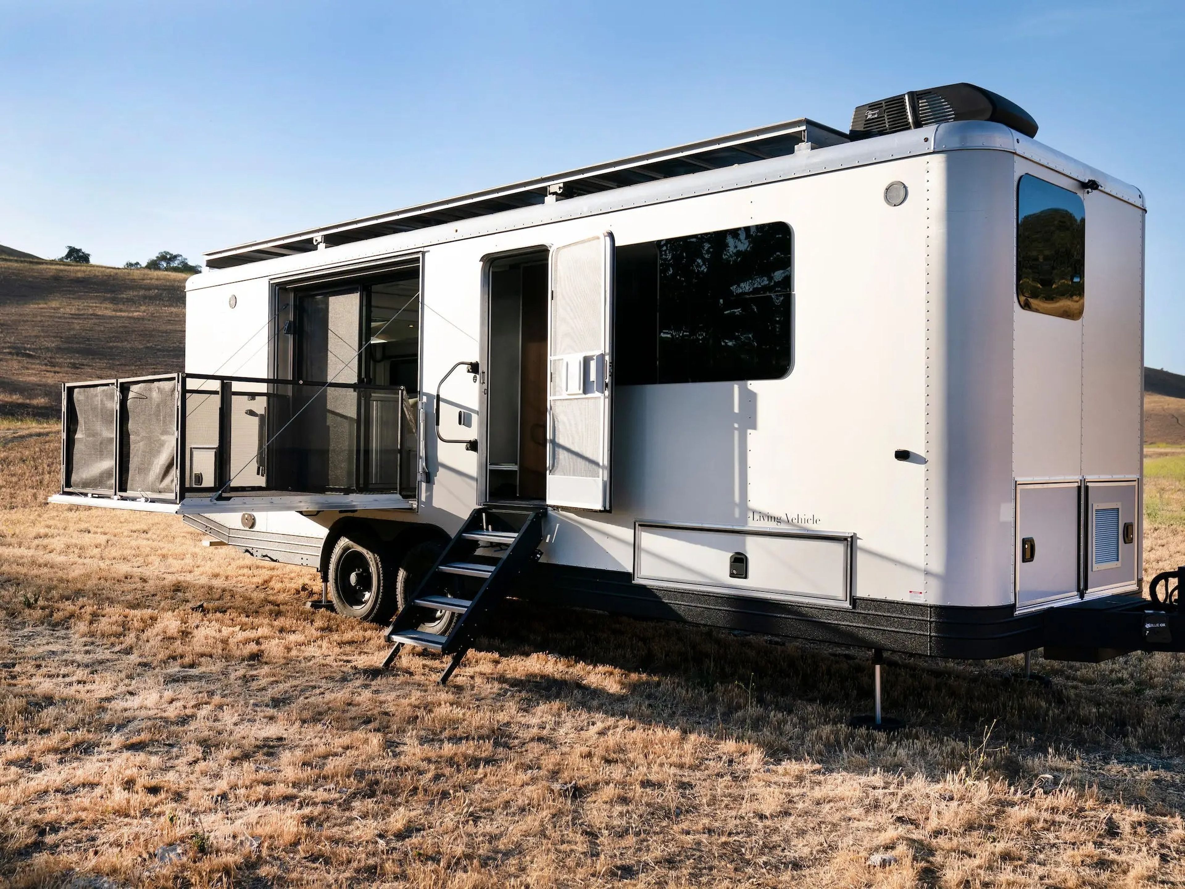 The exterior of the travel trailer as it sits on a brown field. The patio is extended.