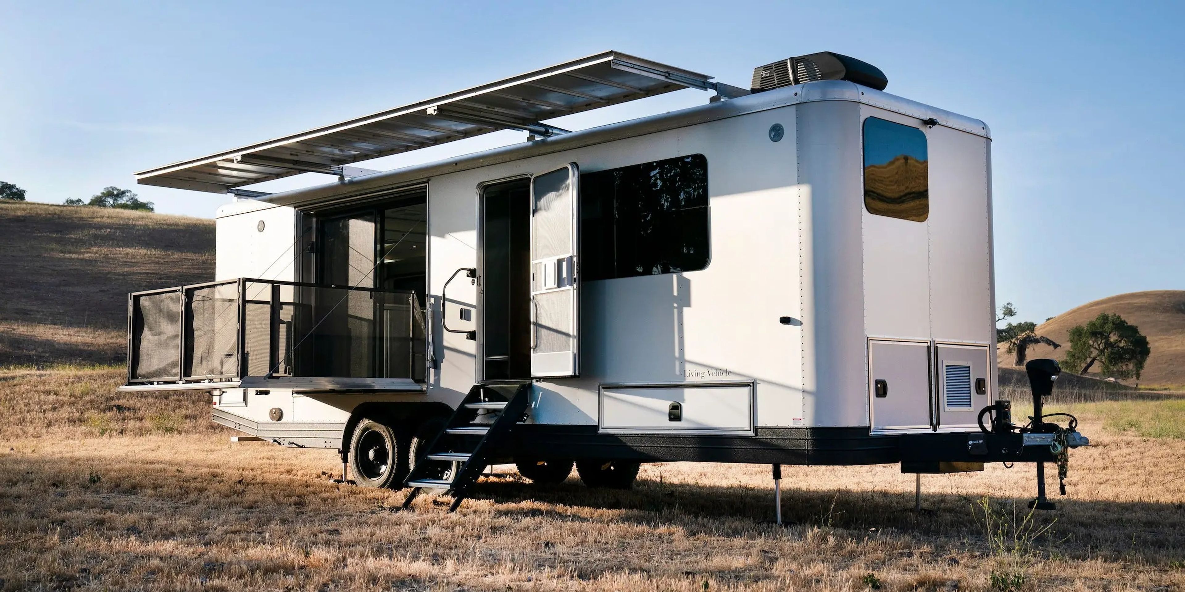The exterior of the travel trailer as it sits on a brown field. The patio is extended.