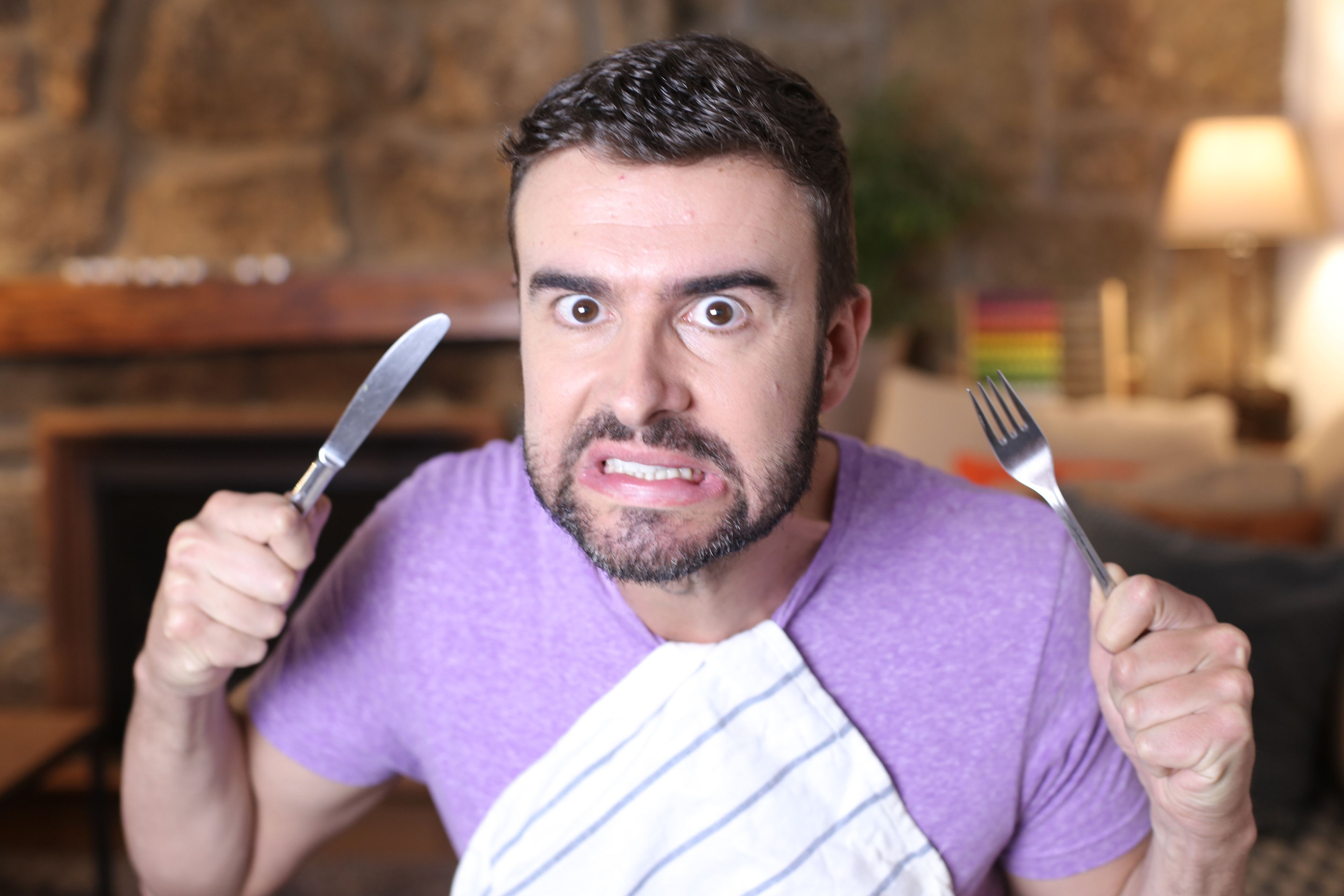 Hombre enfadado sosteniendo cuchillo y tenedor