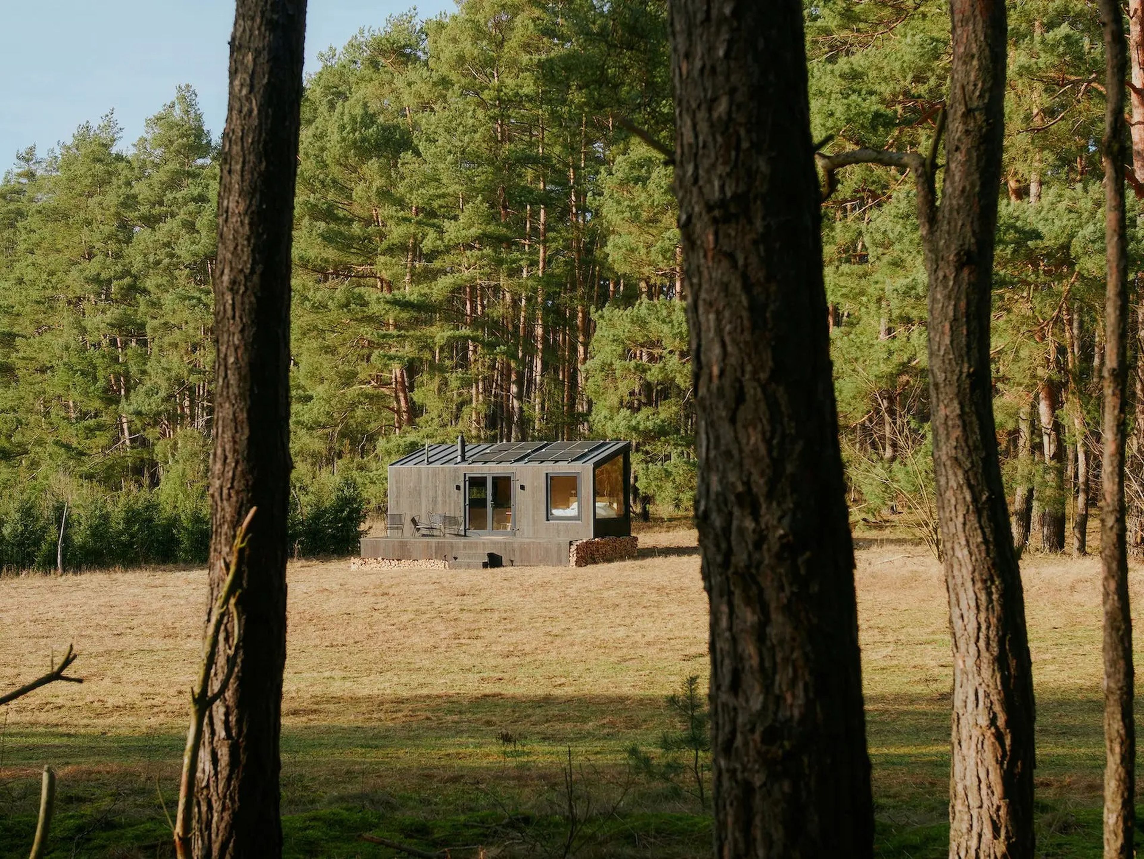 Una cabaña de Raus en la naturaleza rodeada de altos árboles y campos abiertos.