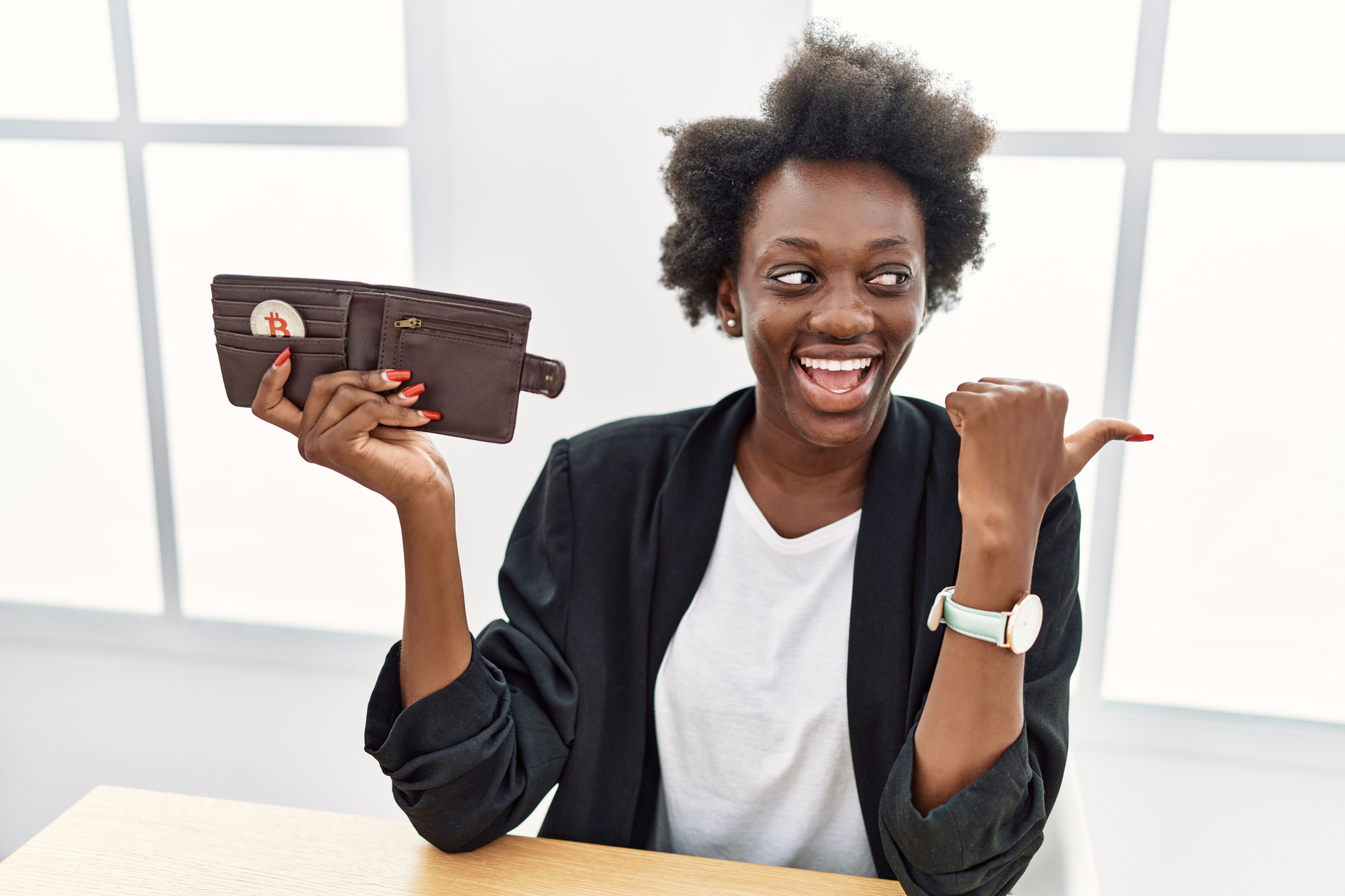 Una mujer muestra con alegría una cartera con una moneda de bitcoin.
