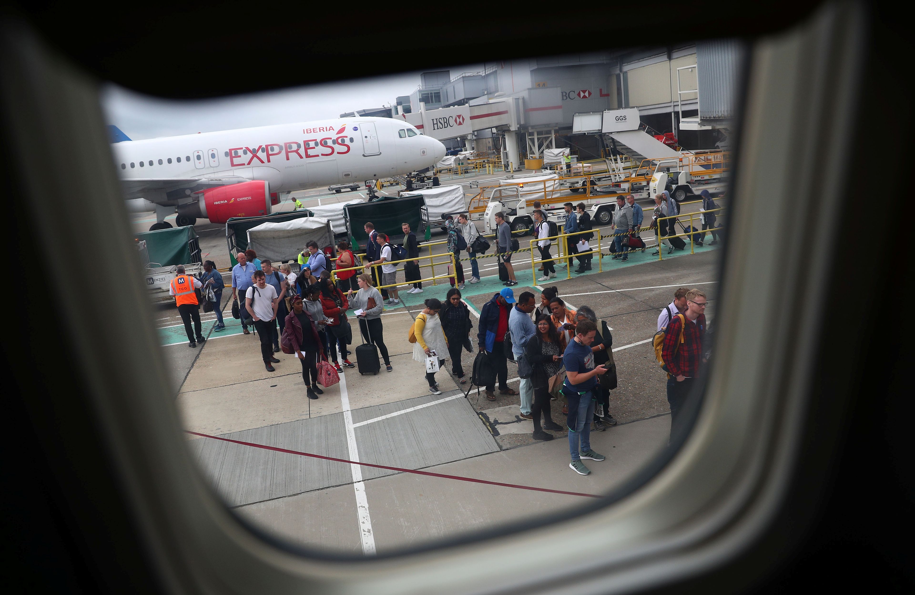Pasajeros esperan para embarcar en un vuelo de Ryanair mientras un avión de Iberia Express espera en su puesto en el aeropuerto de Gatwick en Londres.