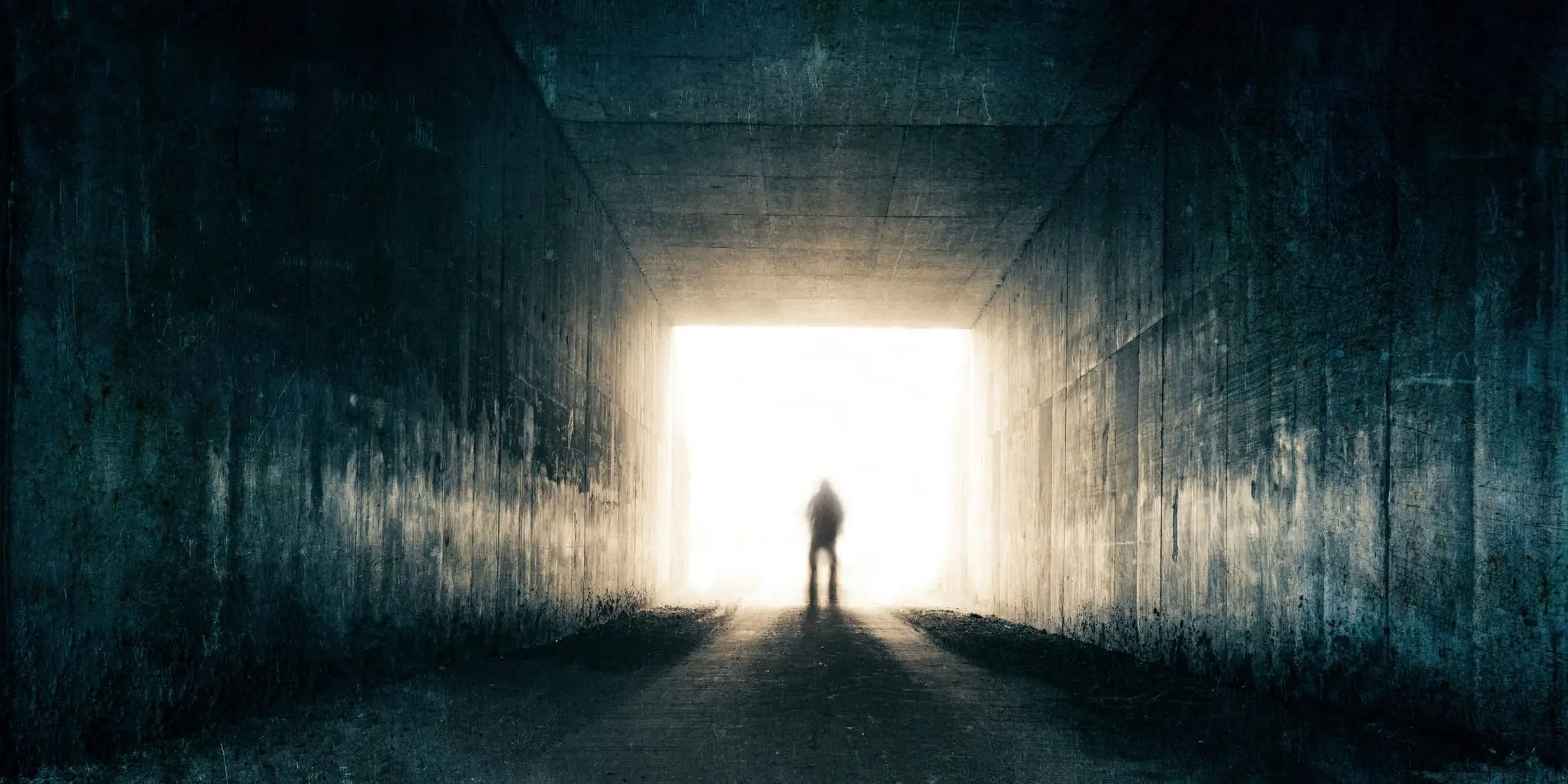 A blurred, threatening figure emerges from the light at the end of a dark sinister tunnel.