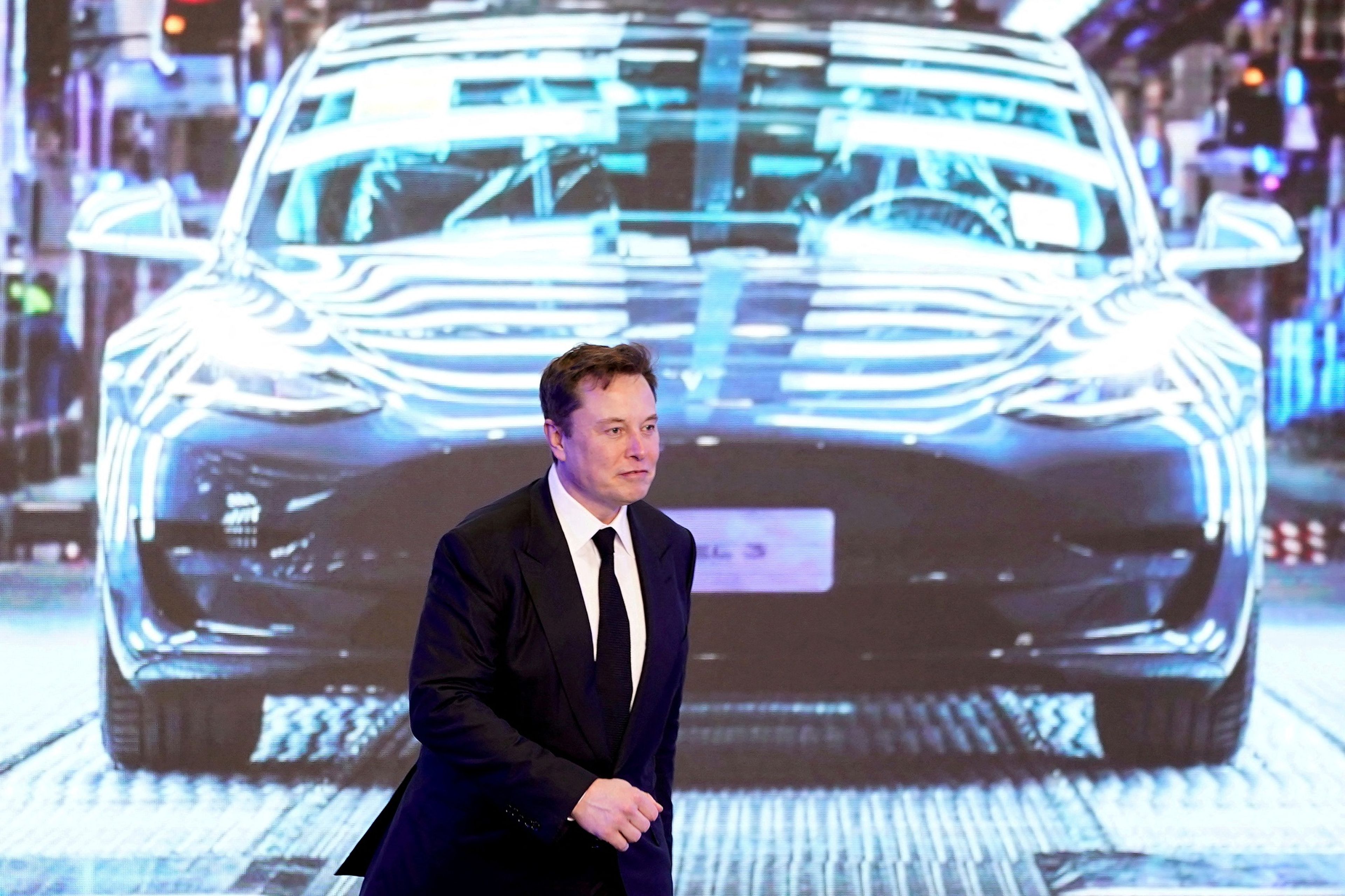 Elon Musk con una foto del Model 3 por detrás en Shanghái.