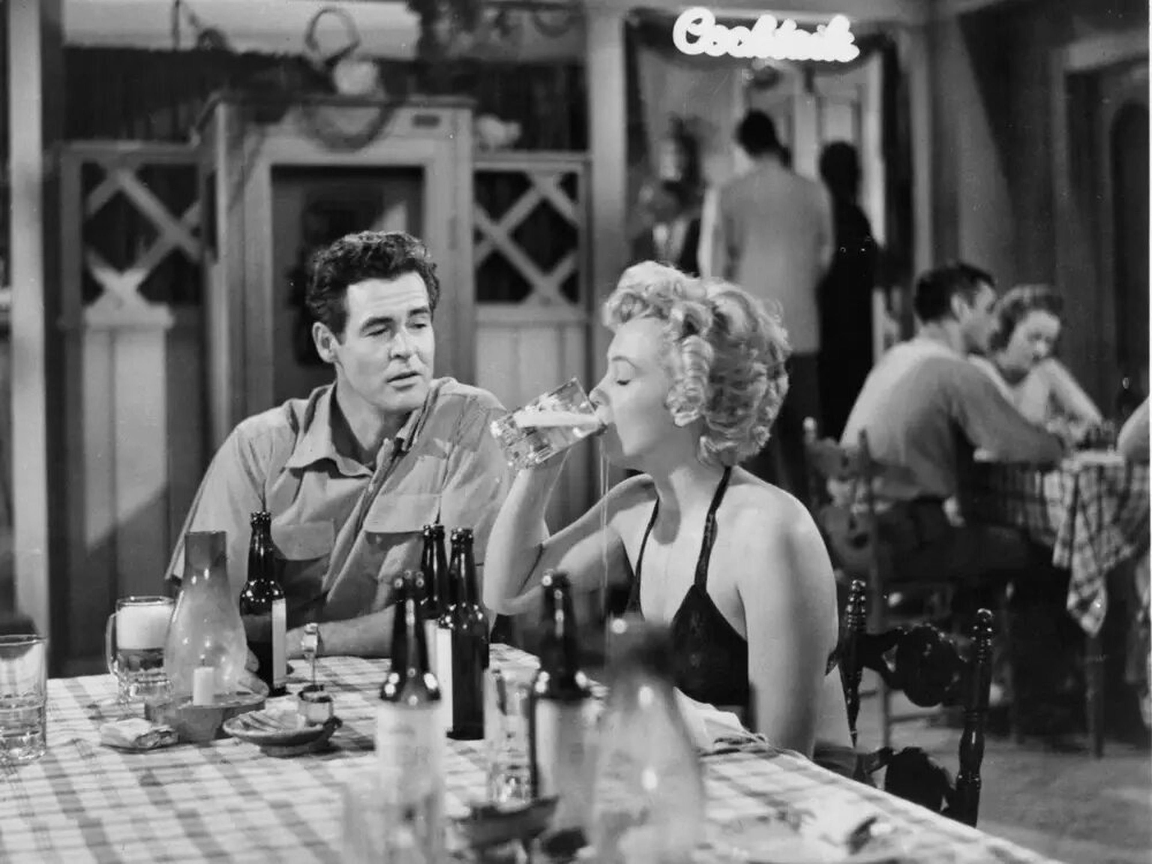 Robert Ryan observa a Marilyn Monroe beber una cerveza en una escena de la película.