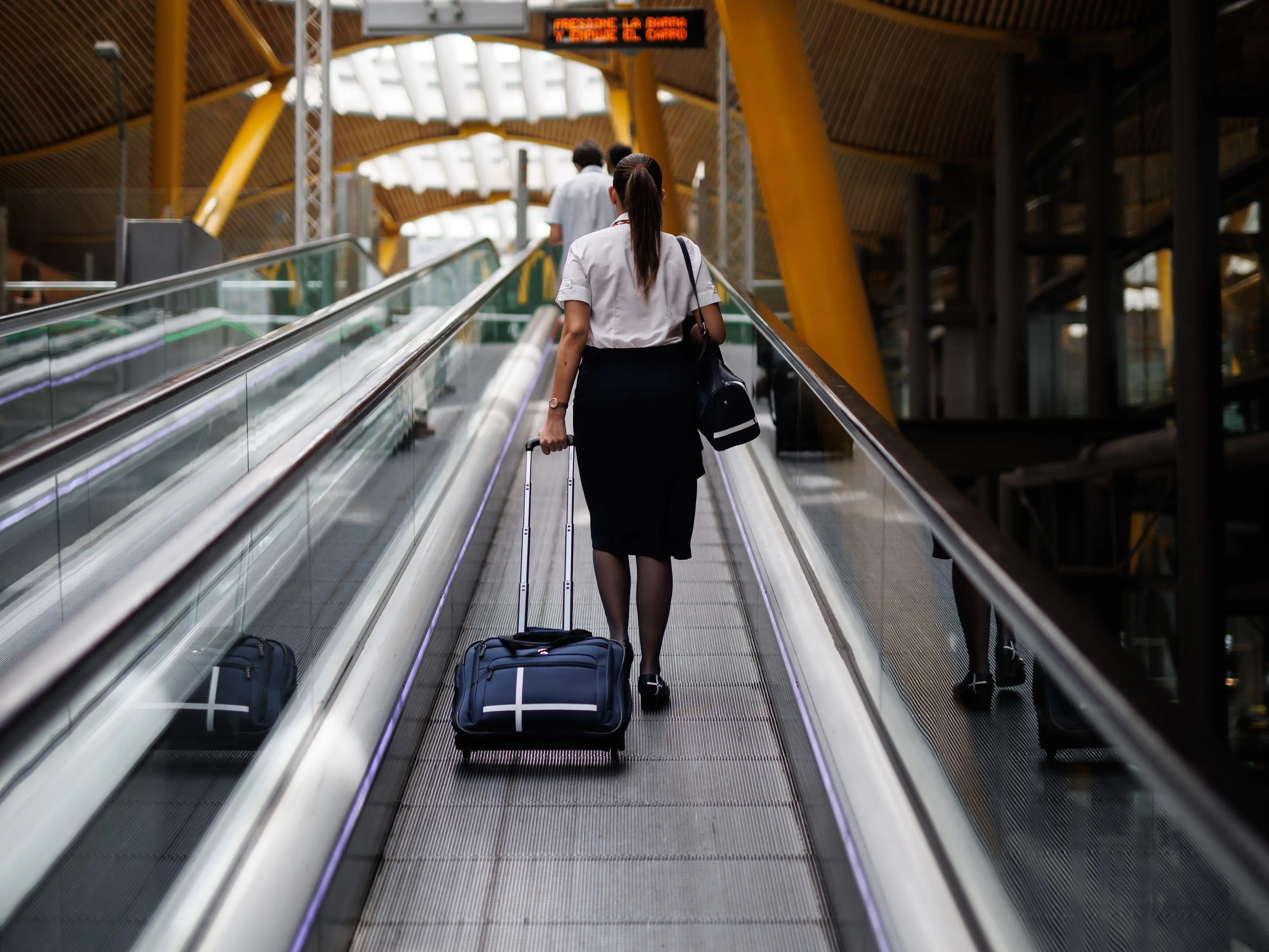 flight attendant riding moving walkway at aiport with suitcase