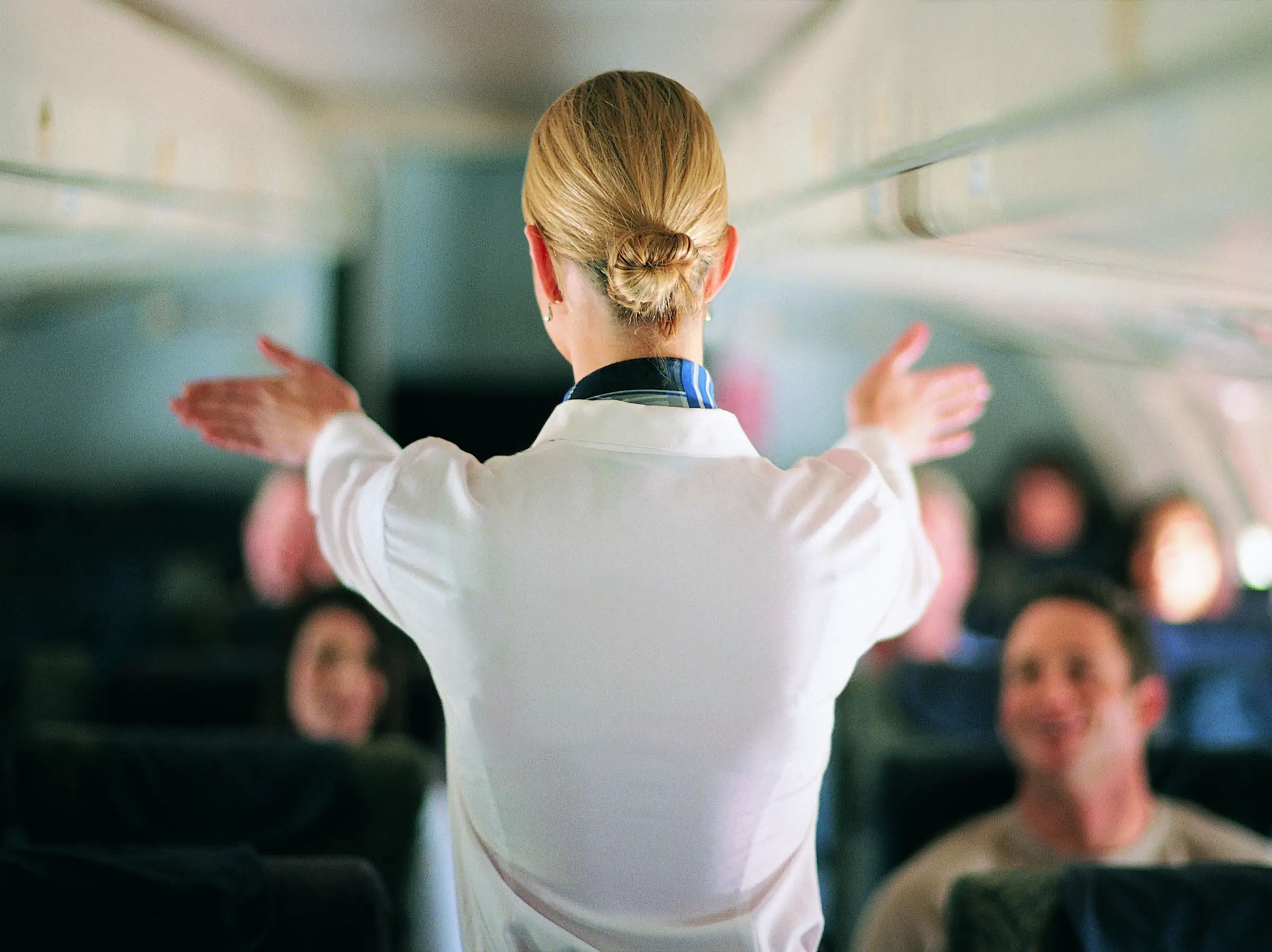 flight attendant standing in plane aisle with hands stretched in front of her