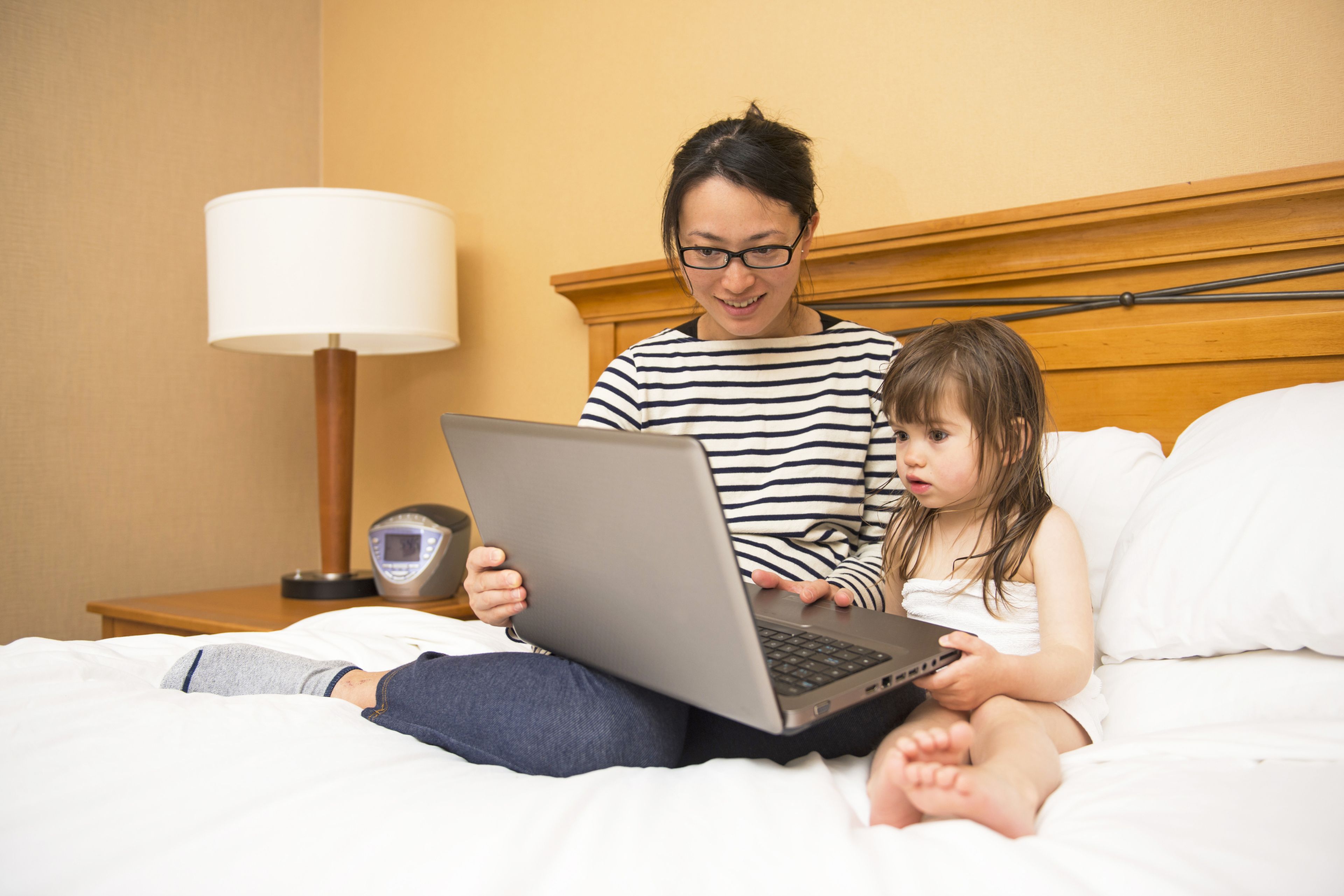 Una madre y su hija con un ordenador encima de la cama.