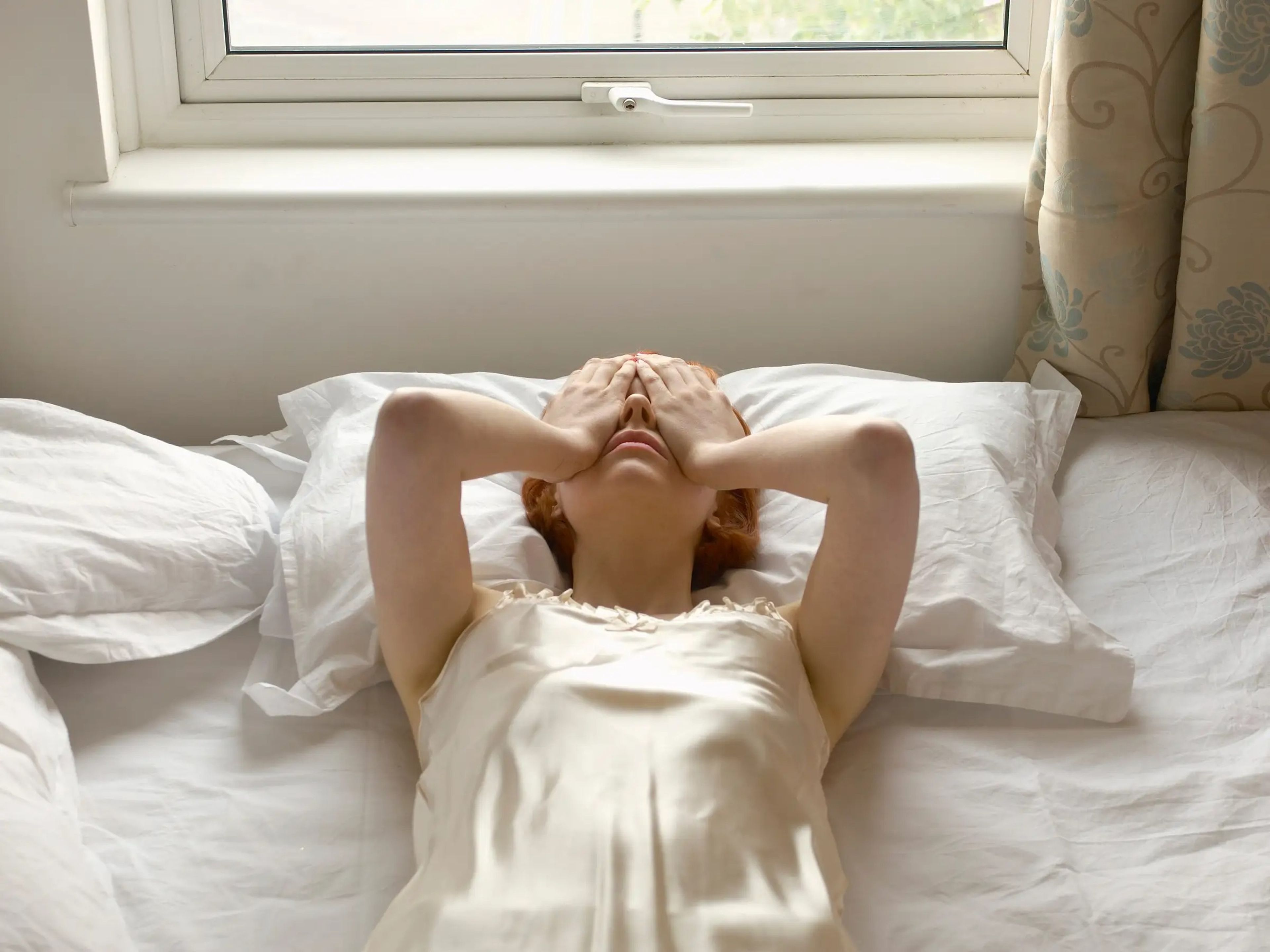 Woman on bed with hands over eyes stock image.