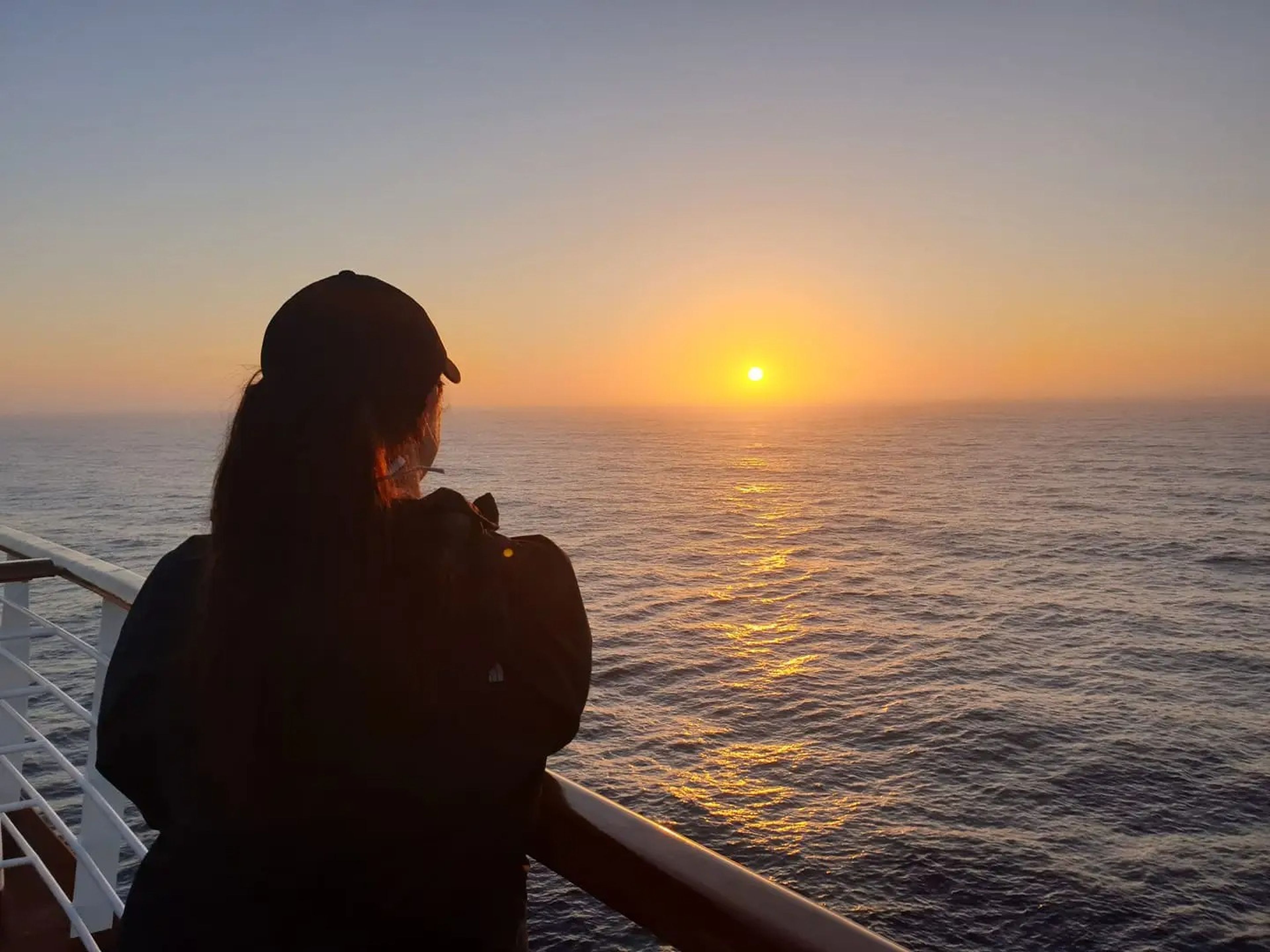 the writer staring over the balcony at a sunset on a cruise