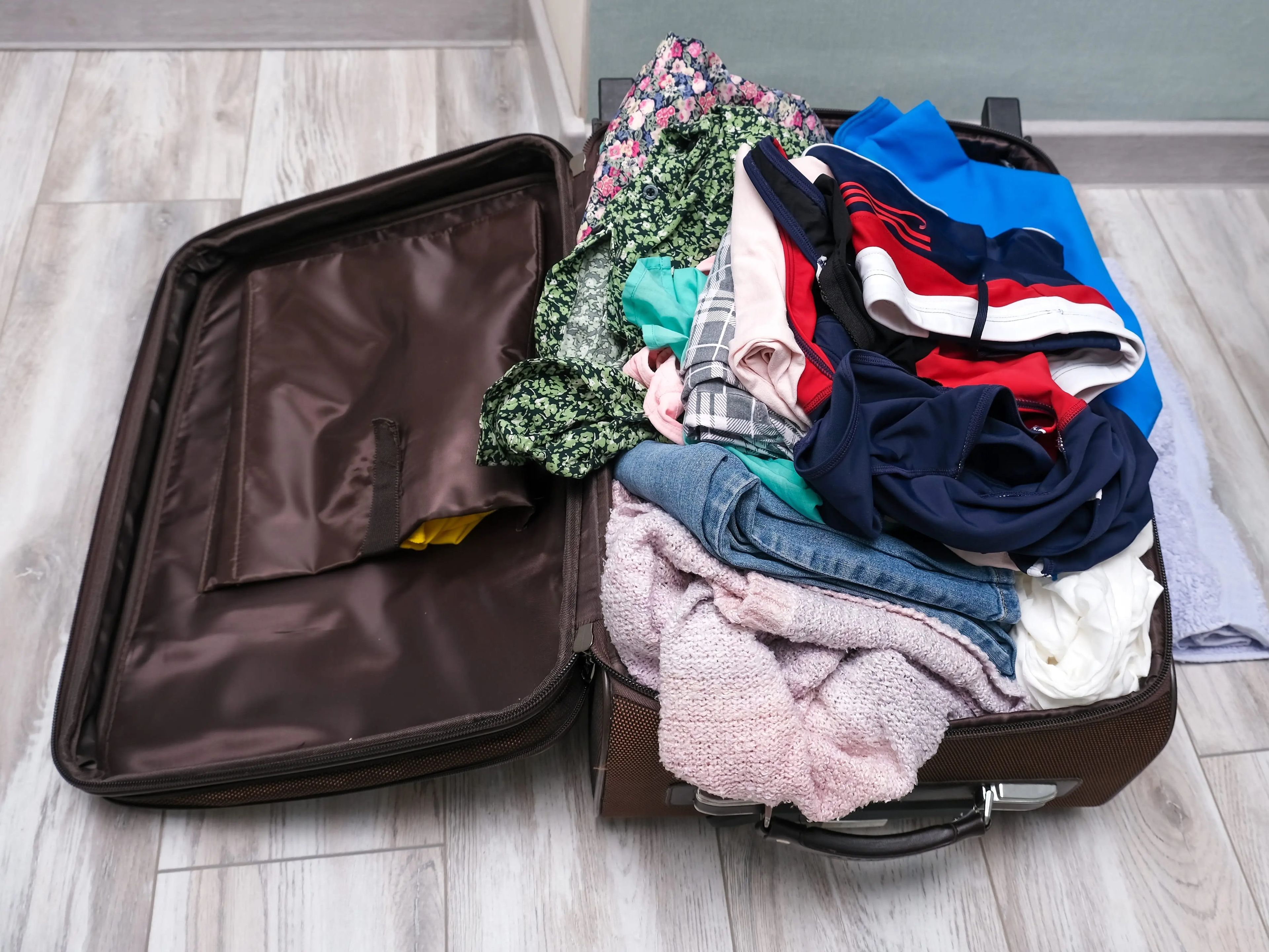 Brown suitcase filled with clothes on gray wooden floors