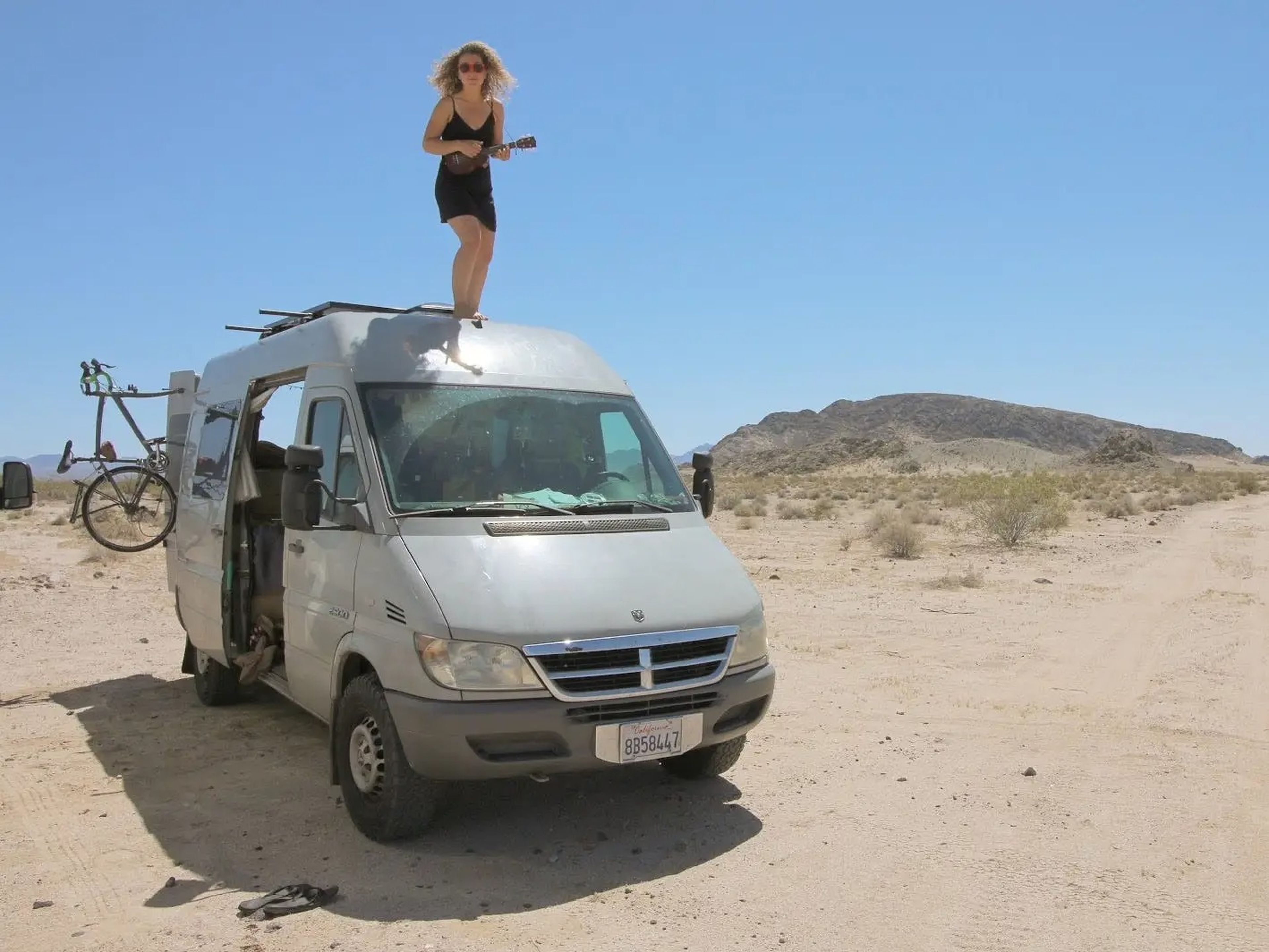 Kaya Lindsay standing ontop of van in desert