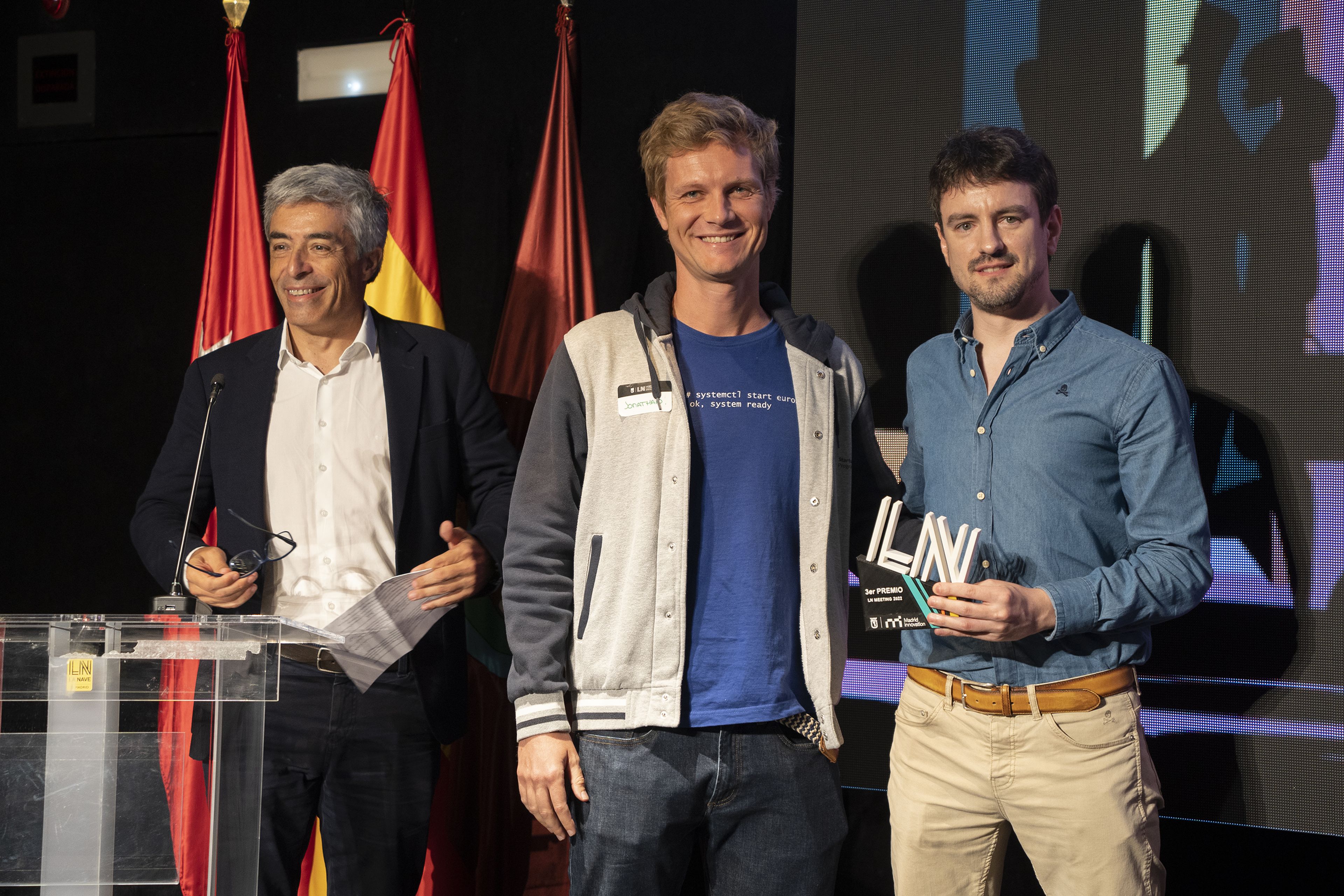 En el centro, Jonathan Clarke entrega un premio a Abel Rodríguez, de Singulary Experts (derecha) en el LN Meeting 2022. A la izquierda, Fernando Herrero, director general de innovación y emprendimiento del Ayuntamiento de Madrid.