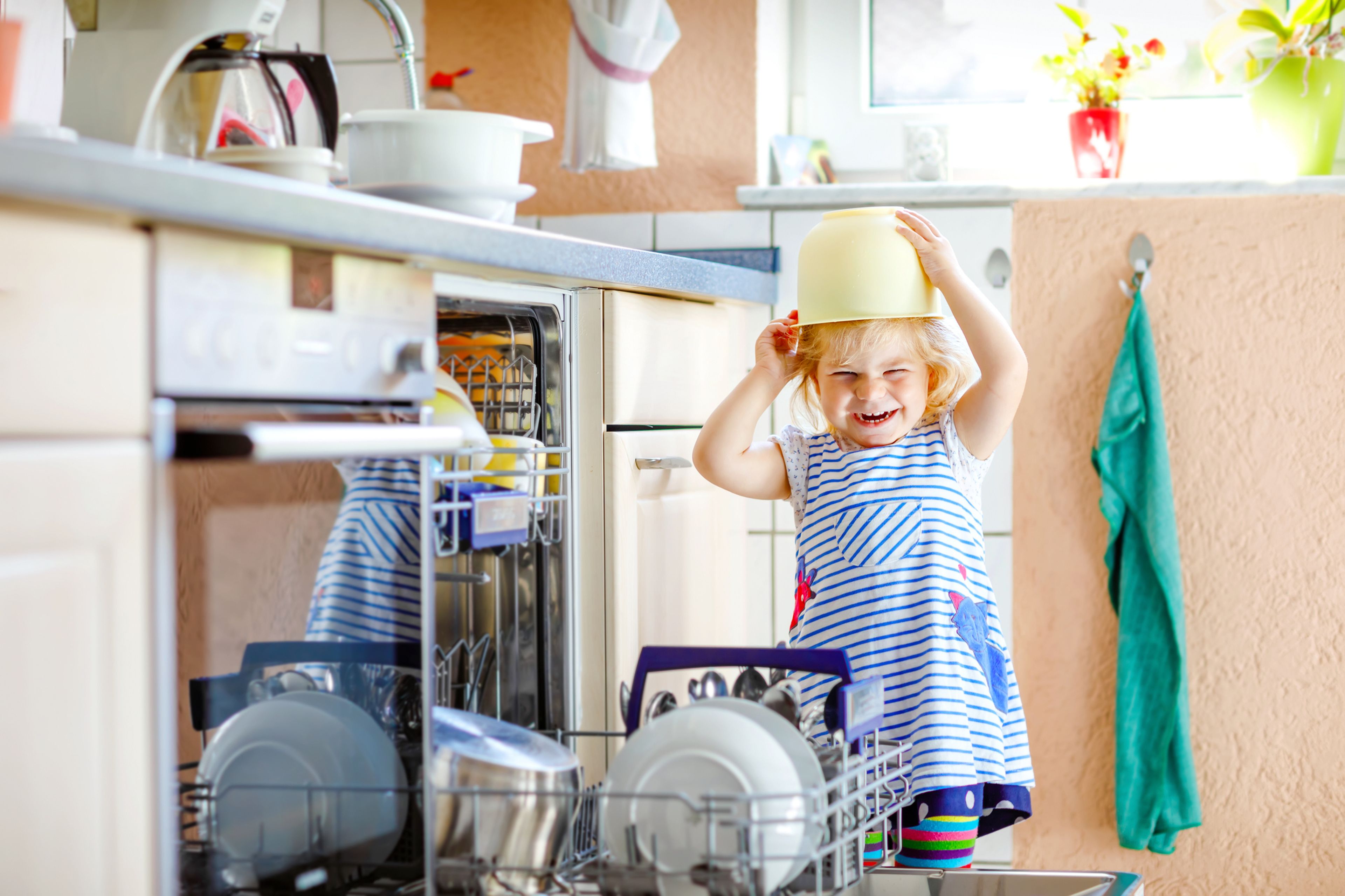 Una niña se pone en la cabeza un bol que ha sacado del lavavajillas.