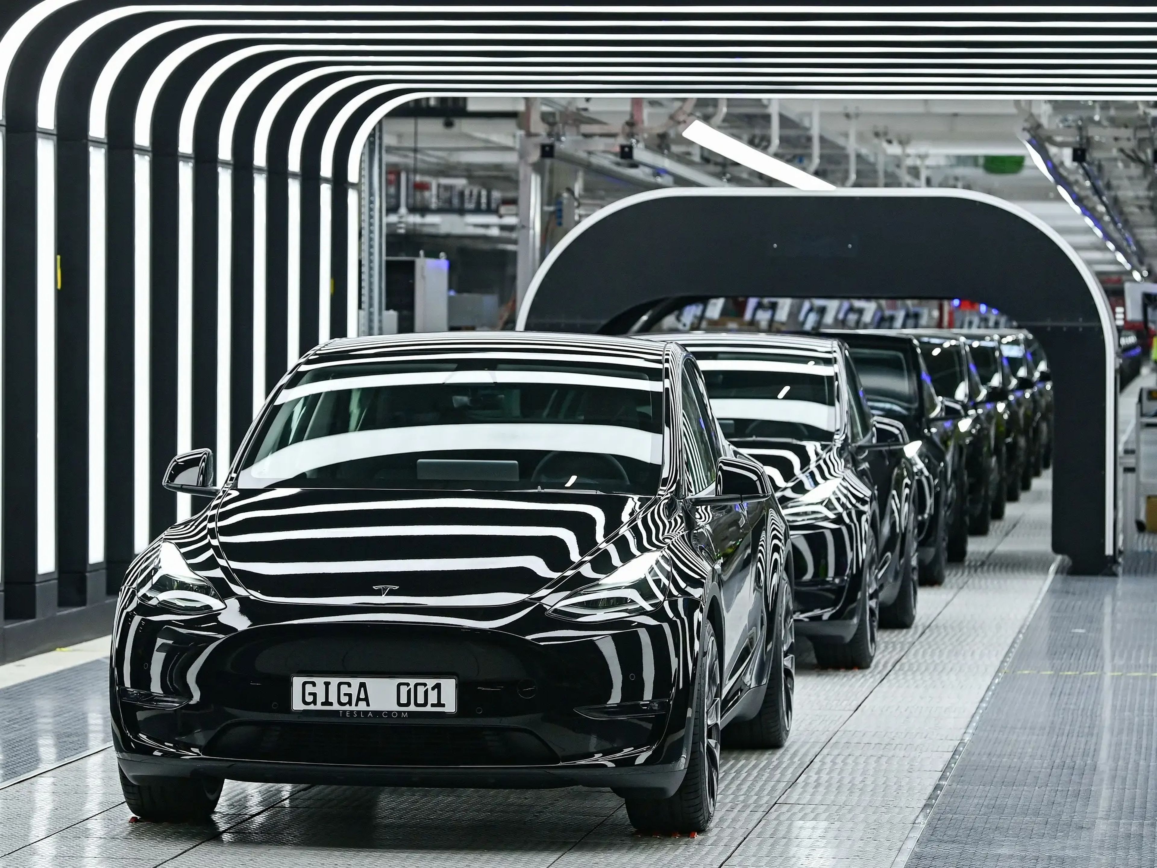 Una fila de coches Tesla sale de una fábrica rodeada de luces.