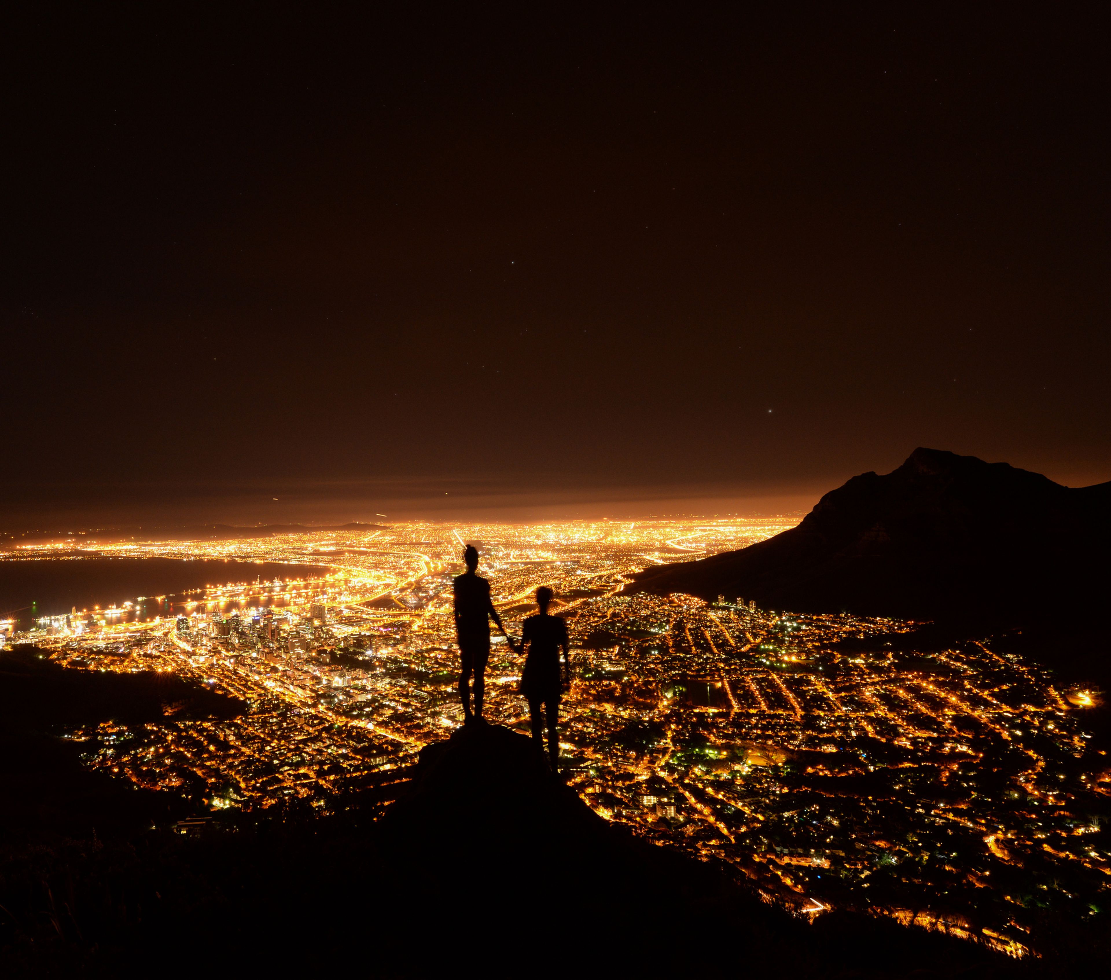 2 personas miran la ciudad iluminada desde lo alto.