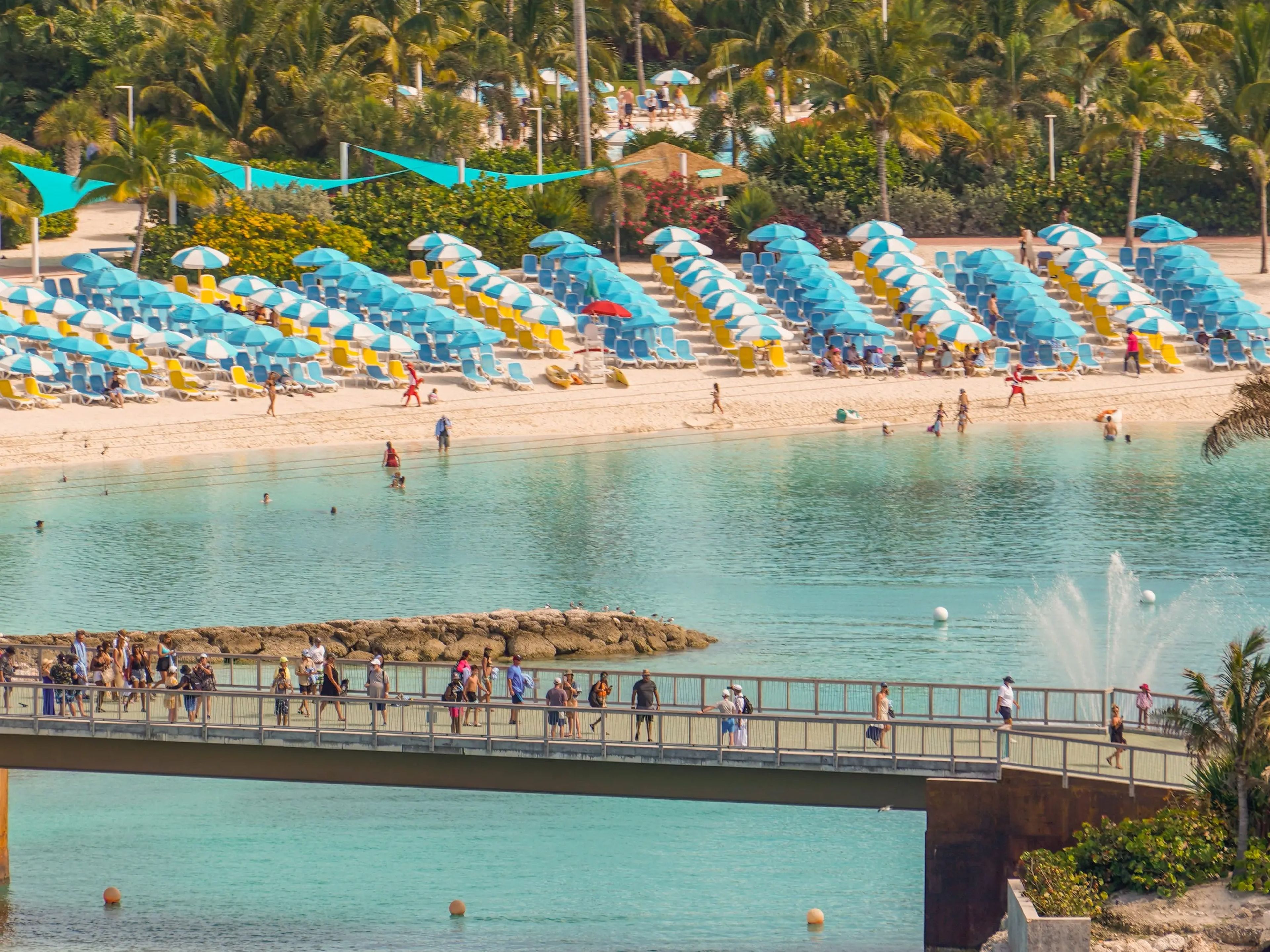 A beach at CocoCay behind a bridge with pedestrians walking across it