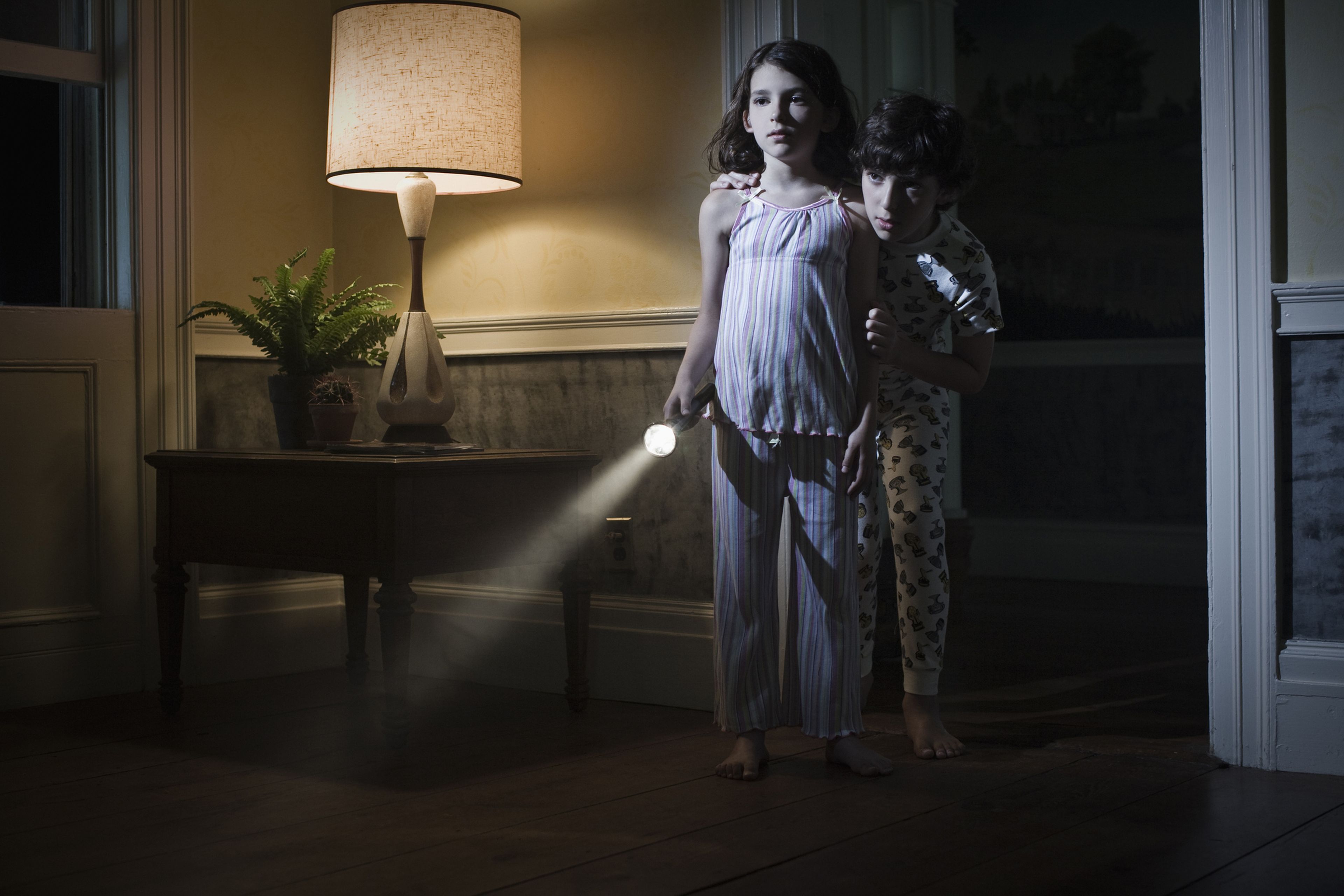Un niño y una niña con una linterna asustados por la noche.