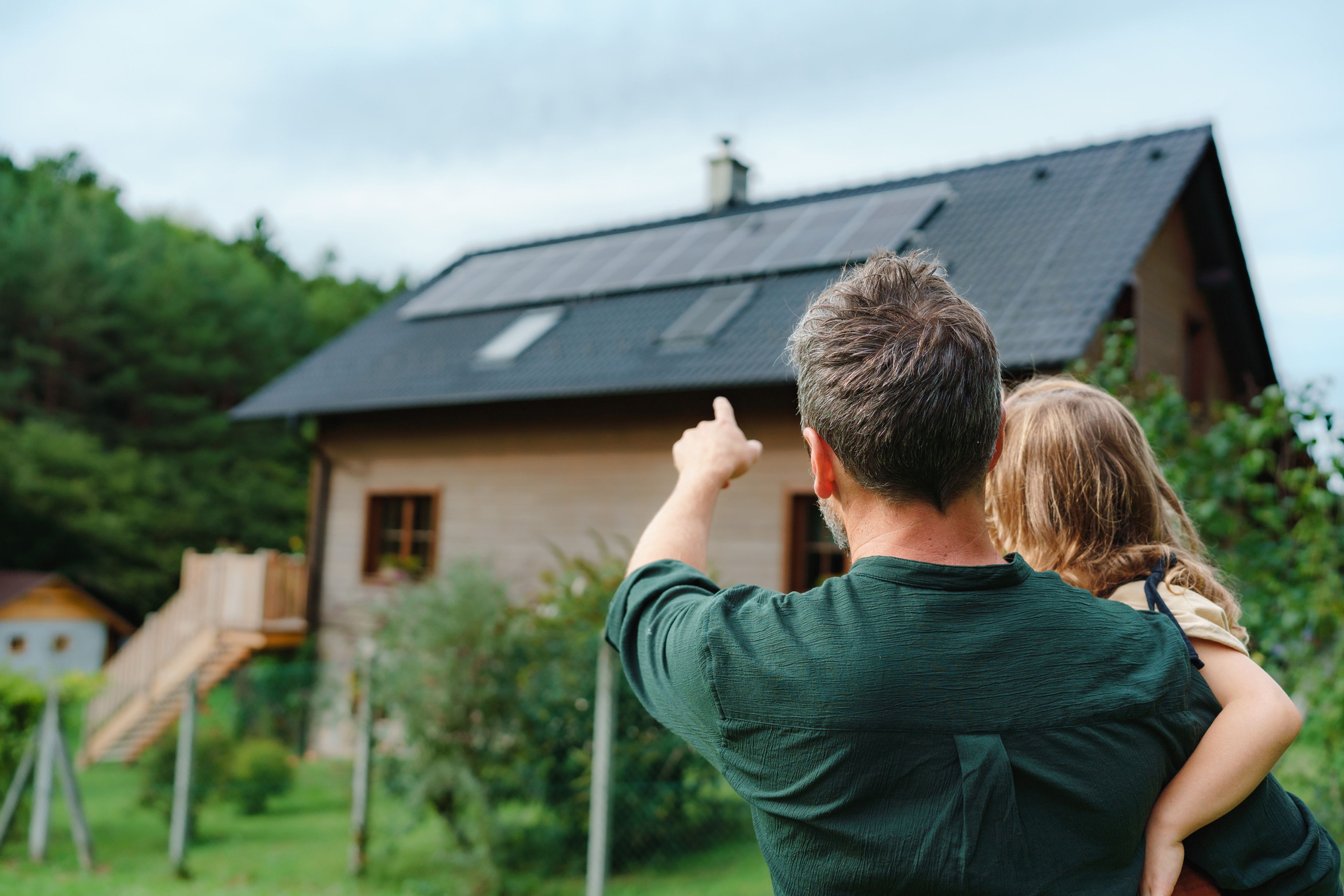 Un padre mira con su hija el tejado de su casa con placas solares.
